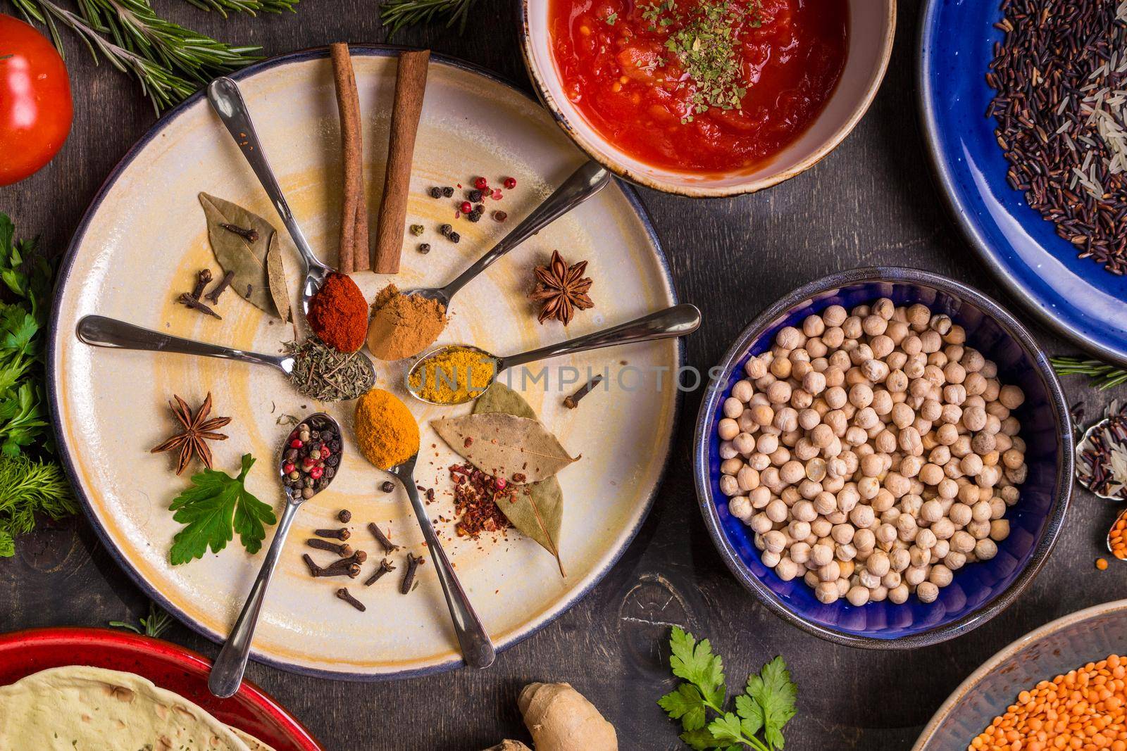 Assorted spices, herbs, chick-pea, lentil, basmati and wild rice mix, tomato chutney and pita on colorful plates. Top view. Spices and different food. Indian/ayurvedic food...