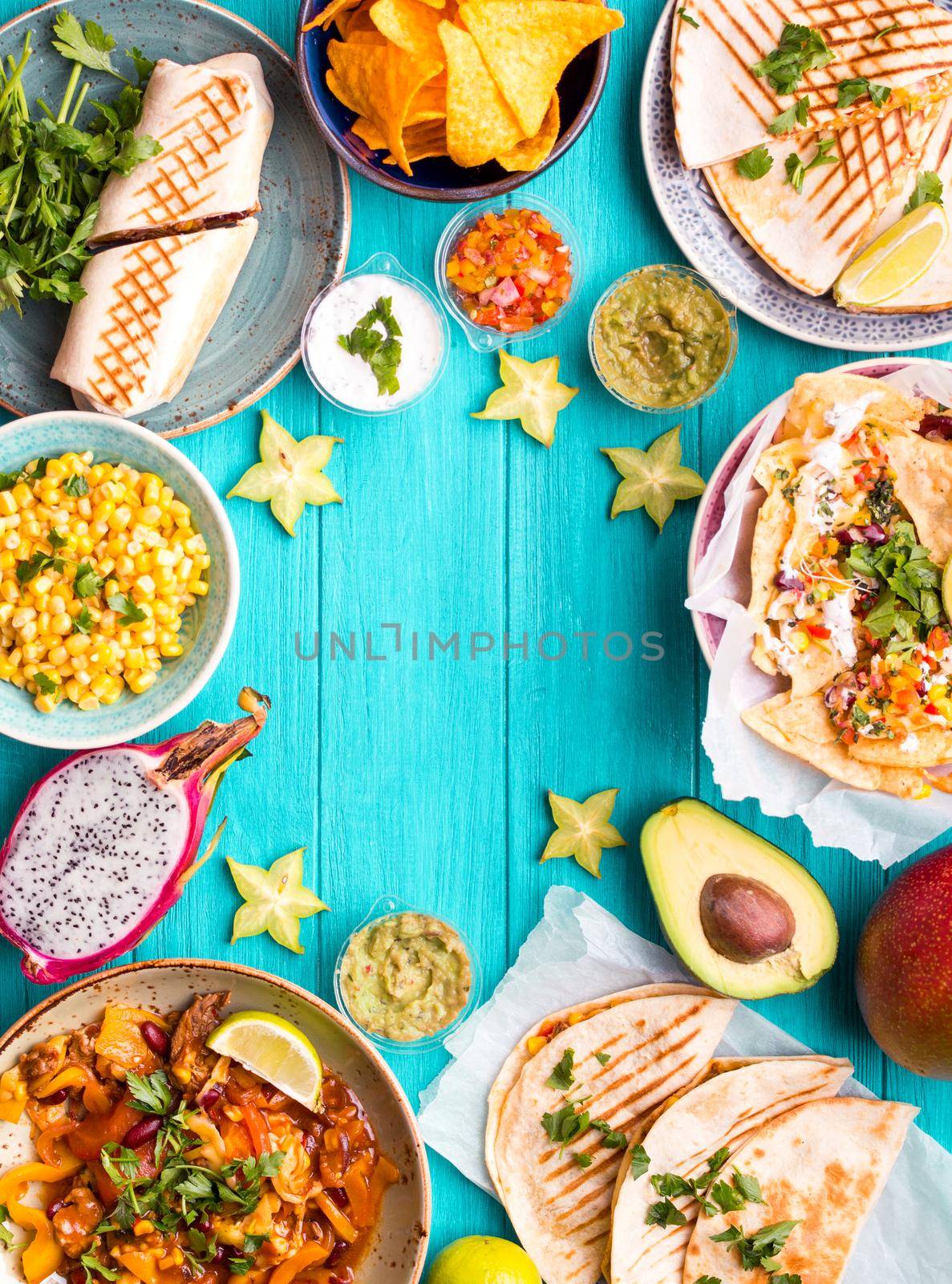 Traditional Mexican food background. Table with different Mexican dishes. Cheese nachos, tacos, guacamole, quesadilla, burrito, fajitas, tortilla chips, Mexican fruits. Tex-Mex cuisine. Space for text