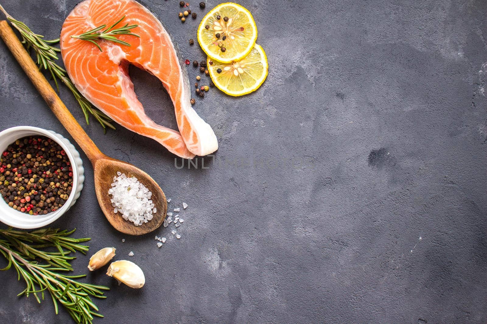 Fresh raw salmon steak, lemon, herbs, spices, wooden spoon on dark rustic concrete background. Food frame. Ingredients set for making healthy dinner. Healthy/diet concept. Space for text. Fresh fish