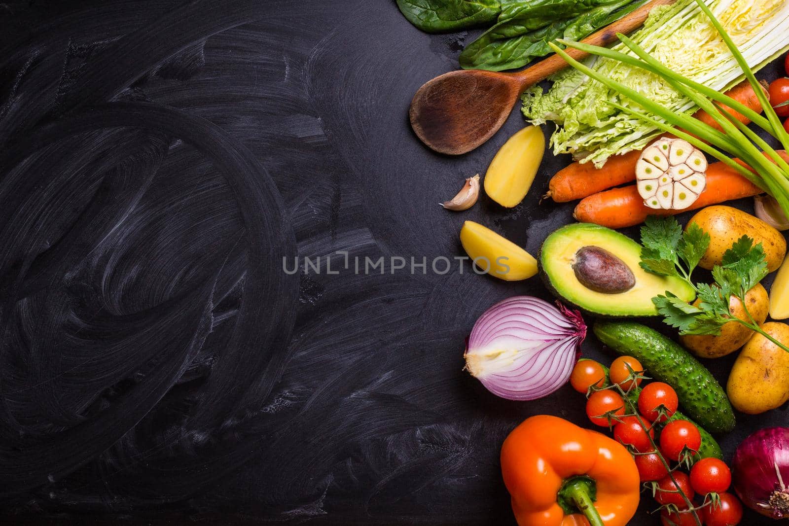 Vegetables, herbs, raw ingredients for cooking and wooden spoon on rustic black chalk board background. Healthy, clean eating concept. Vegan or gluten free diet. Space for text. Top view. Salad making