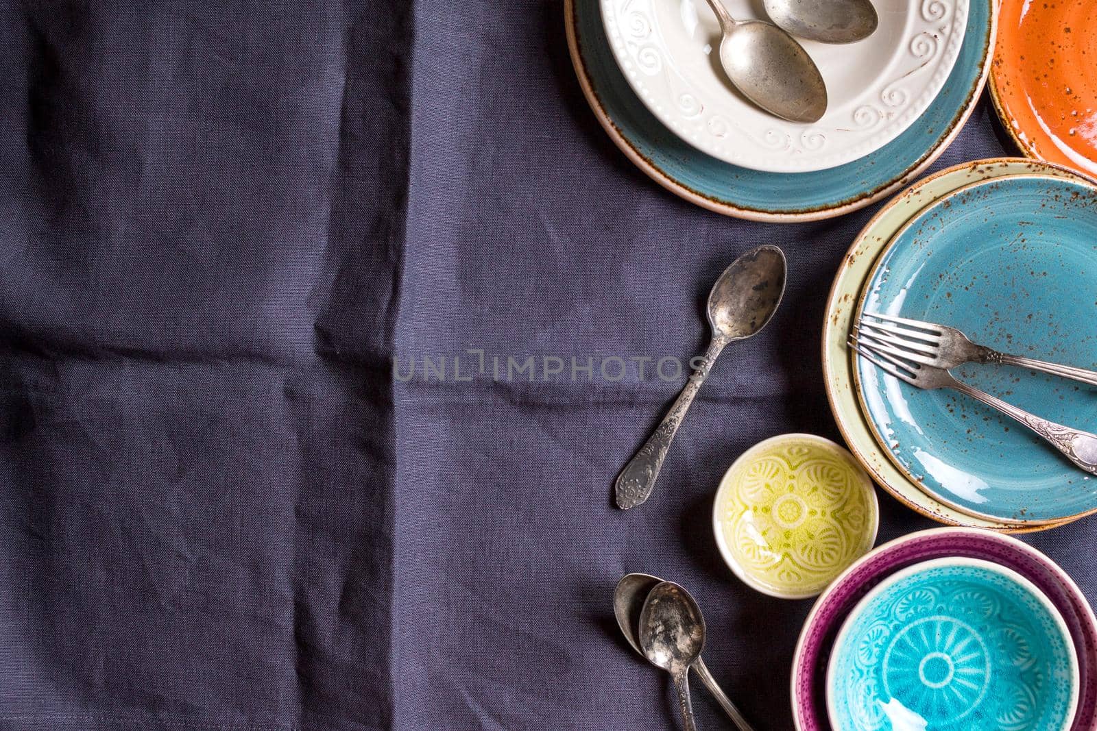 Vintage multicolored empty plates and bowls on a gray linen tablecloth. With antique spoons and forks. Space for text. Table setting. Shabby chic/retro style. Top view. Rustic kitchen. Copy space