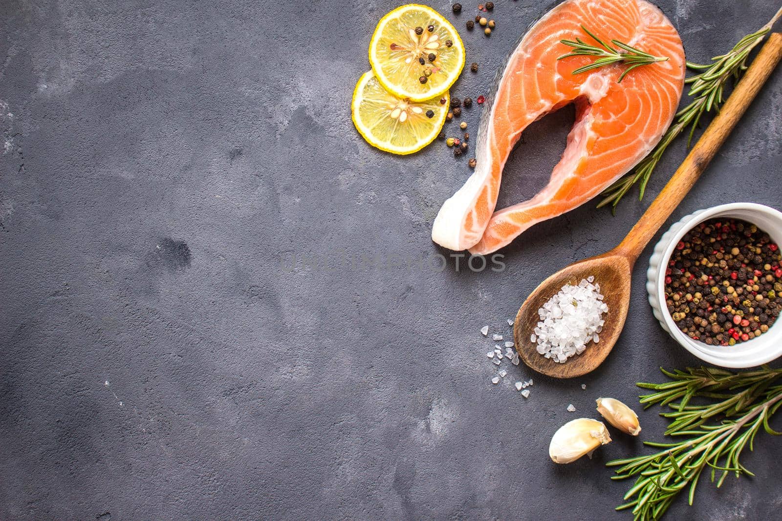 Fresh raw salmon steak, lemon, herbs, spices, wooden spoon on dark rustic concrete background. Food frame. Ingredients set for making healthy dinner. Healthy/diet concept. Space for text. Fresh fish