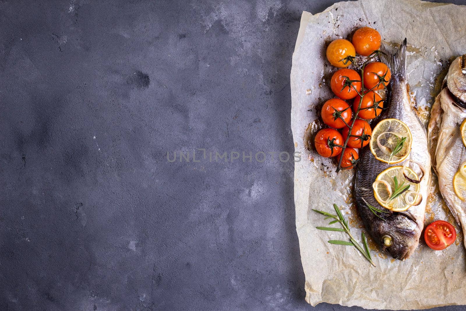 Tasty baked fish on dark rustic background. Baked sea bream with lemon, onion, herbs, tomatoes, spices. Space for text. Grilled delicious fish background. Diet and healthy food concept. Top view