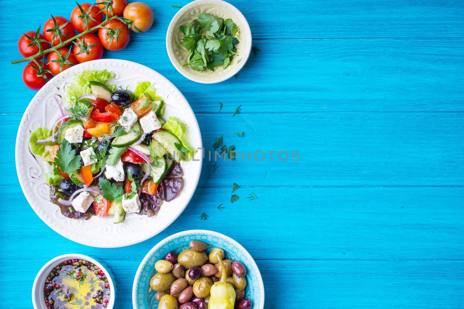 Greek salad background. Bowl with fresh greek salad, tomatoes, olives, olive oil on wooden table. Space for text. Top view. Traditional greek dish. Ingredients for making salad. Mediterranean diet