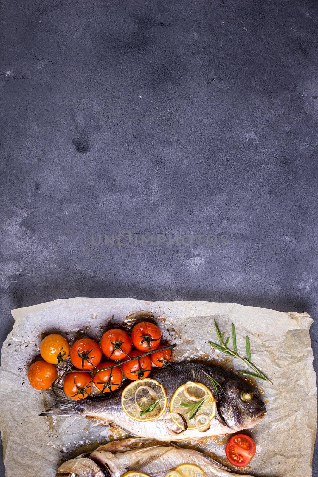 Tasty baked fish on dark rustic background. Baked sea bream with lemon, onion, herbs, tomatoes, spices. Space for text. Grilled delicious fish background. Diet and healthy food concept. Top view