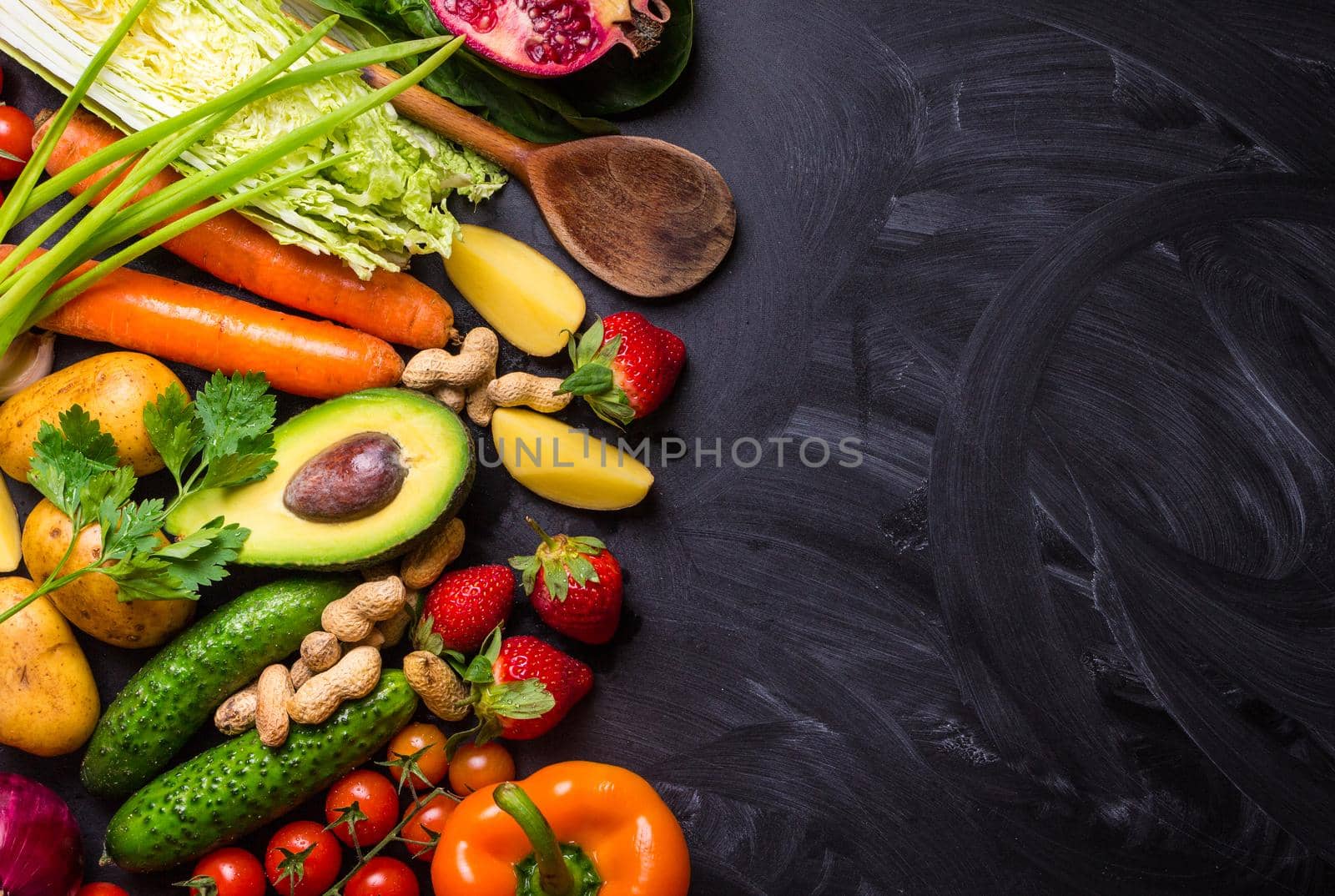 Vegetables, fruits, herbs, raw ingredients for cooking and spoon on rustic black chalk board background. Healthy, clean eating concept. Vegan or gluten free diet. Space for text. Top view. Food frame