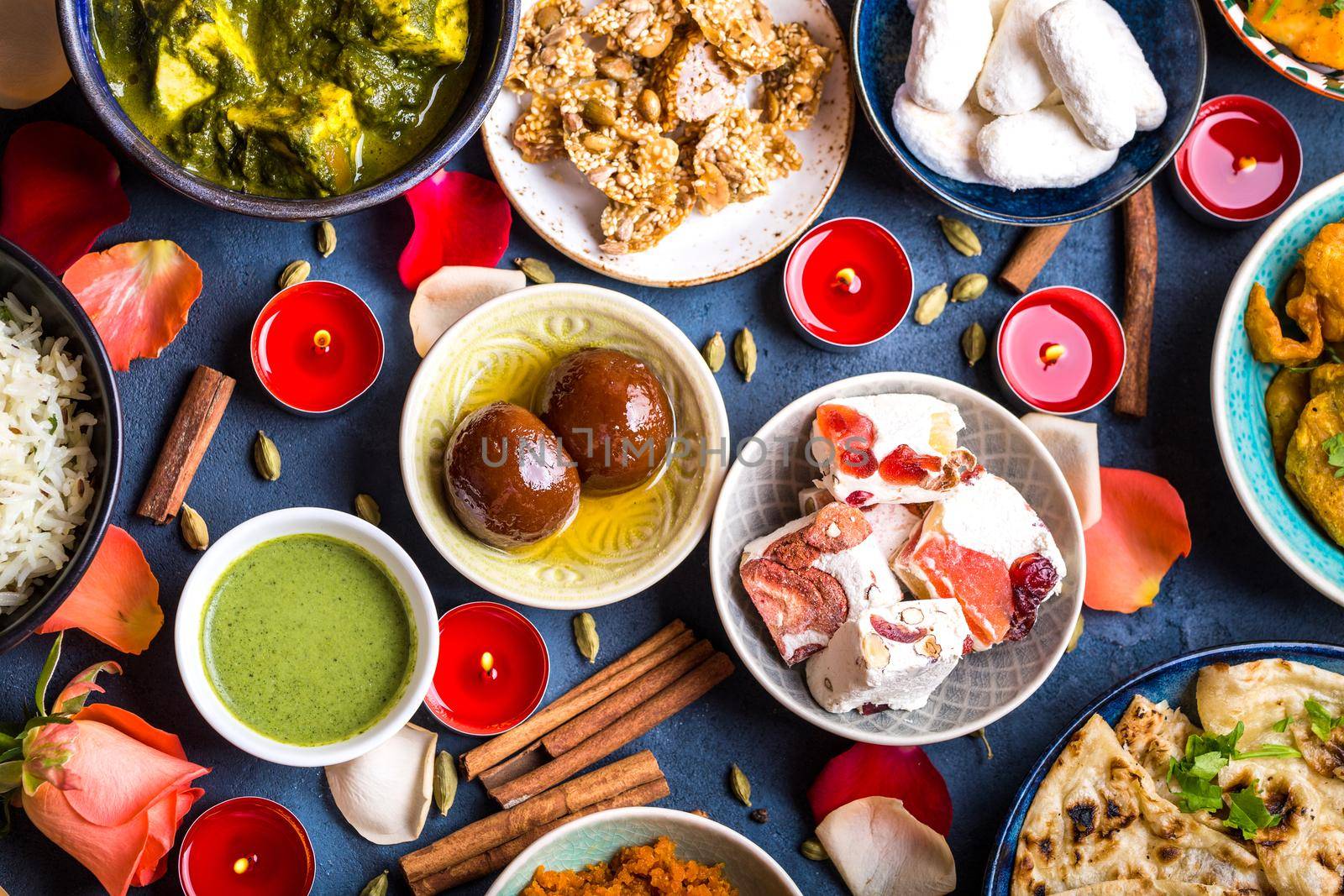 Festive food for Indian festival Diwali. Close-up. Naan, samosa, rice, paneer, sweets. Holiday Indian table with food, sweets, flowers, burning candles. Diwali celebratory dinner. Assorted Indian food