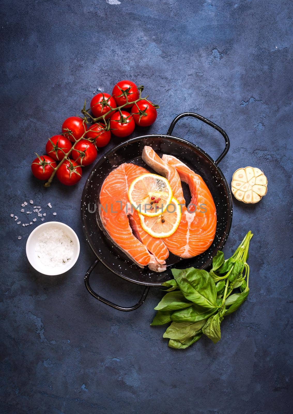 Raw fresh fish with vegetables ready to cook. Raw salmon steaks with lemon, spices and herbs in a pan. Ingredients for cooking on a rustic concrete background. Diet and healthy food. Fish for dinner