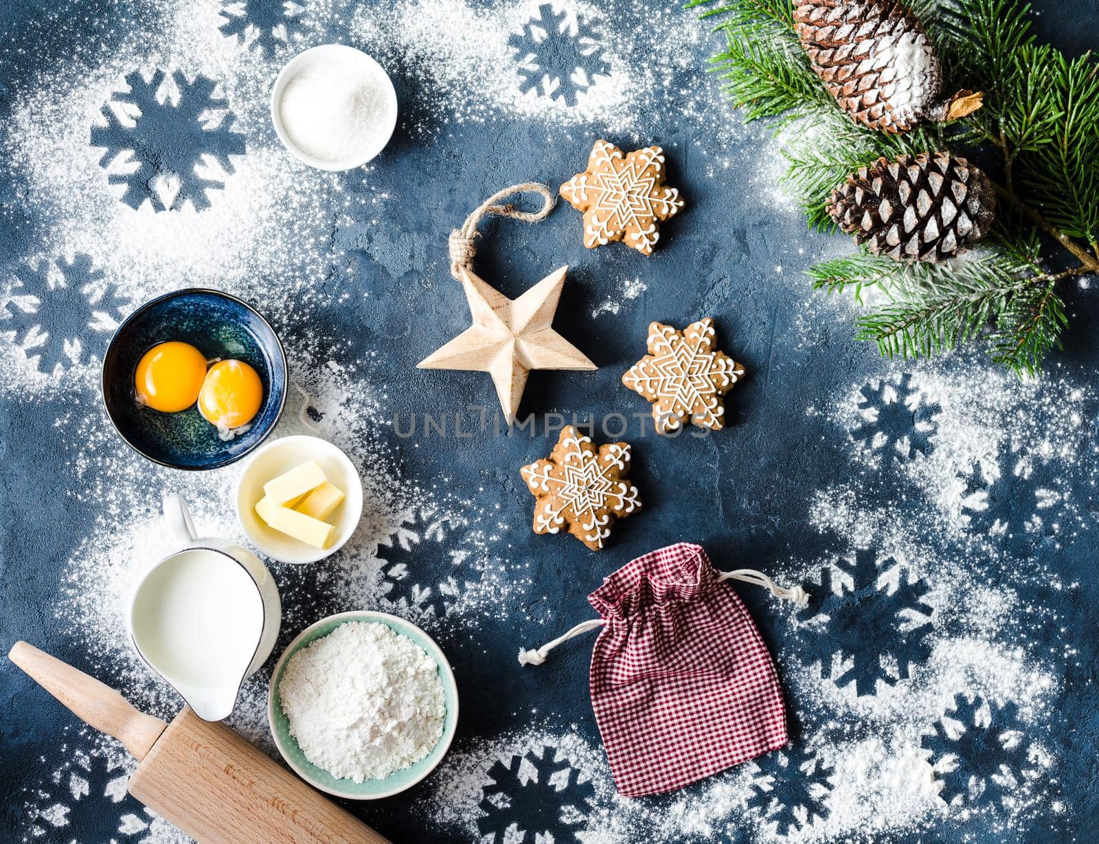 Christmas/New Year food background. Baking ingredients, snowflake cookies, Christmas decoration, gift bag. Making festive New Year sweets. Flour, rolling pin, gingerbread, milk, eggs. Top view.