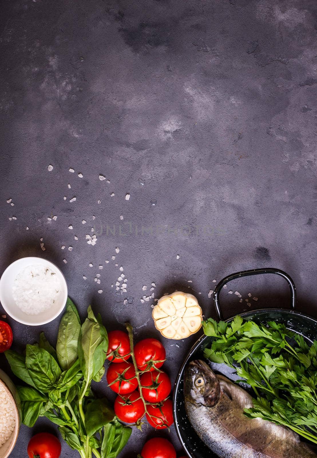 Raw fresh whole fish with vegetables and rice ready to cook. Fresh trout on a pan. Ingredients for cooking on a gray concrete background. Space for text. Diet and healthy food concept. Fish background