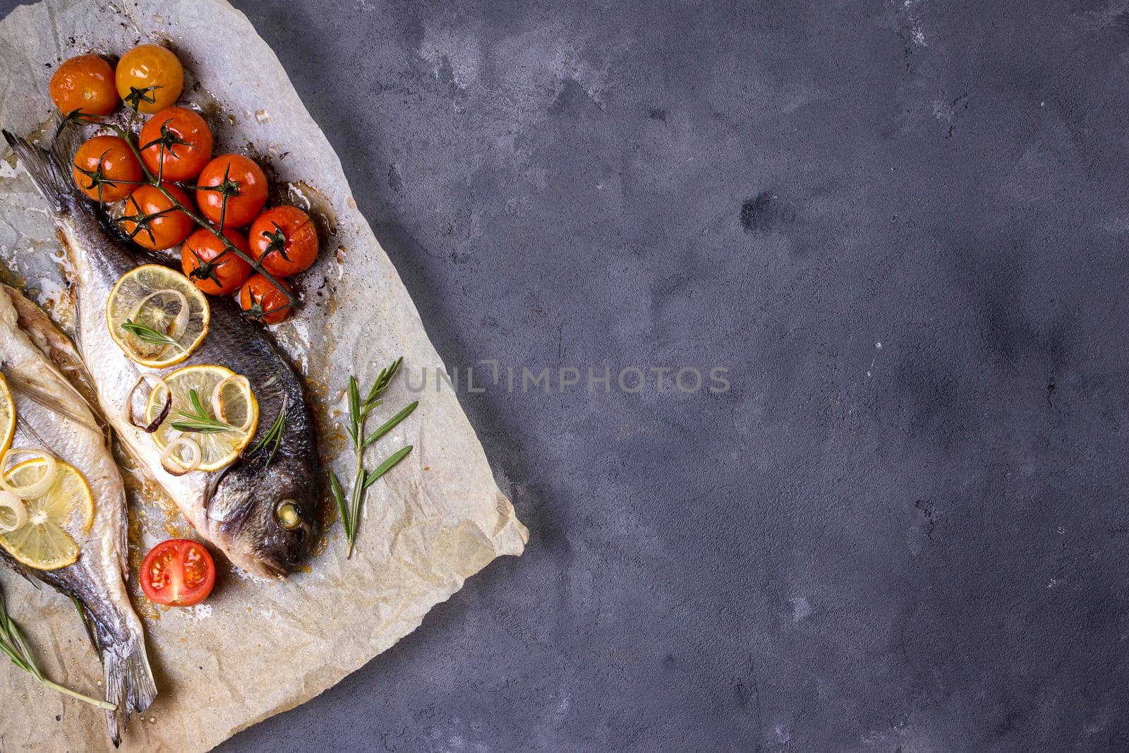 Tasty baked fish on dark rustic background. Baked sea bream with lemon, onion, herbs, tomatoes, spices. Space for text. Grilled delicious fish background. Diet and healthy food concept. Top view