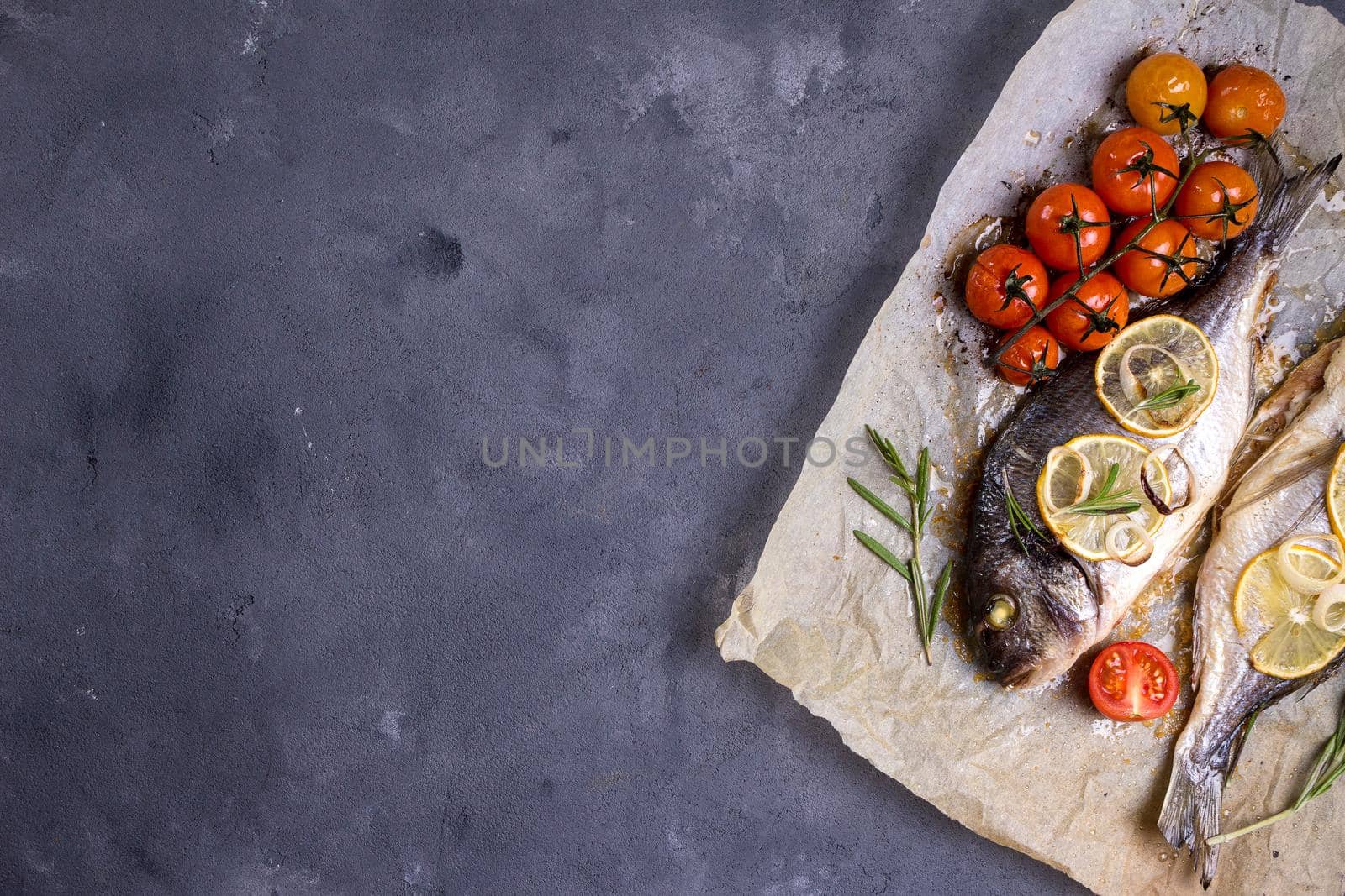 Tasty baked fish on dark rustic background. Baked sea bream with lemon, onion, herbs, tomatoes, spices. Space for text. Grilled delicious fish background. Diet and healthy food concept. Top view