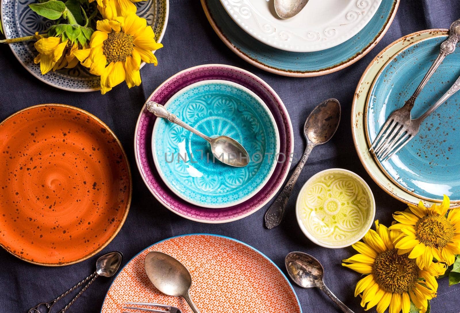 Vintage multicolored empty plates and bowls on a dark gray linen tablecloth with sunflower. With antique spoons and forks. Table setting. Shabby chic/retro style. Top view. Rustic kitchen