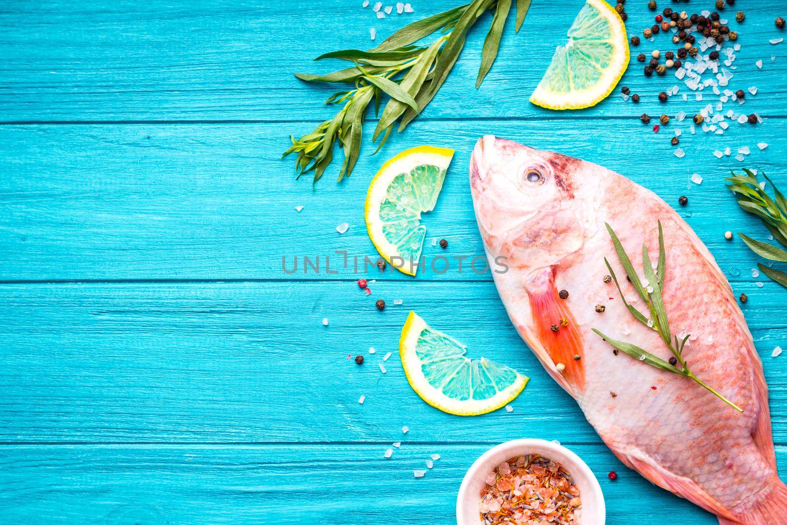 Fresh fish tilapia ready to cook. Raw fish with herbs, lemon, salt, pepper on wooden rustic background. Ingredients for cooking or making healthy dinner. Fish background. Space for text. Diet/healthy