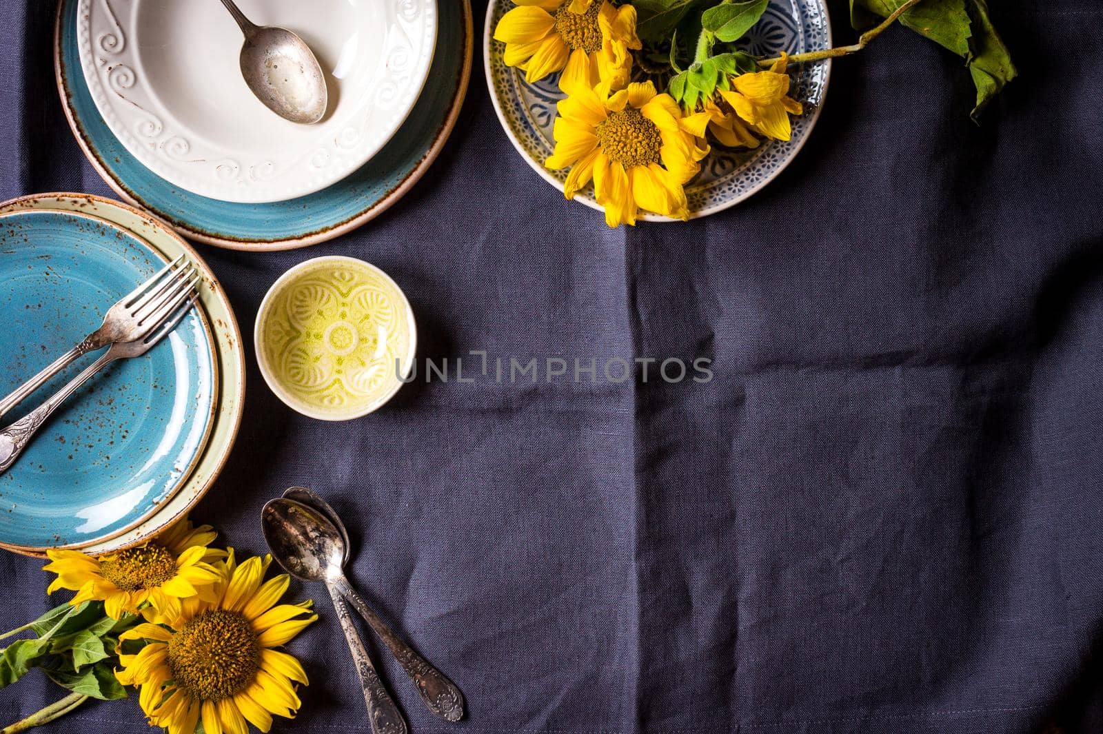 Vintage multicolored empty plates and bowls on a dark gray linen tablecloth with sunflower. With antique spoons and forks. Space for text. Table setting. Shabby chic/retro style. Top view. Copy space