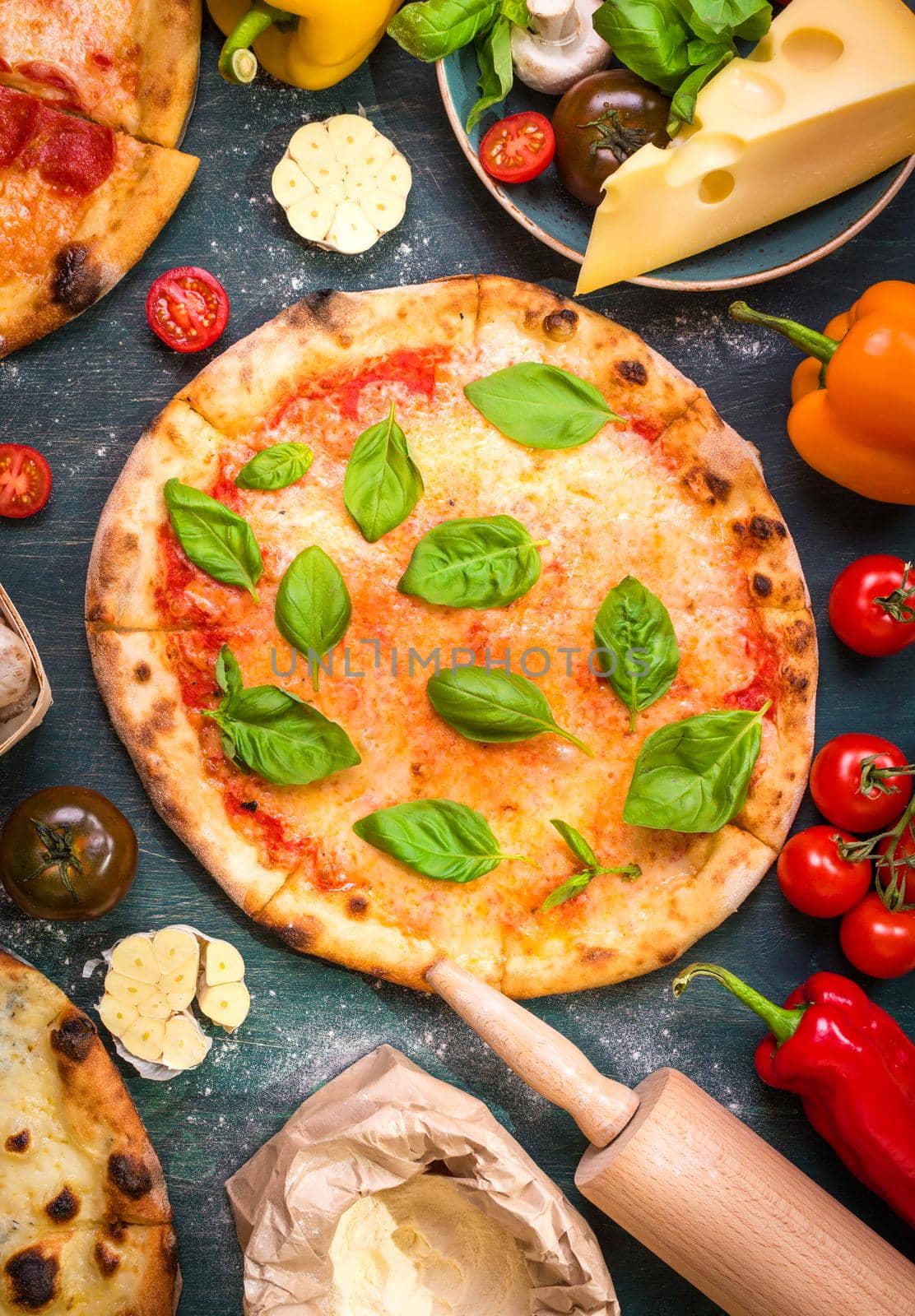 Delicious baked pizza and ingredients for making pizza. Flour, cheese, tomatoes, basil, pepperoni, mushrooms and rolling pin over wooden background. Top view. Pizza ready to eat