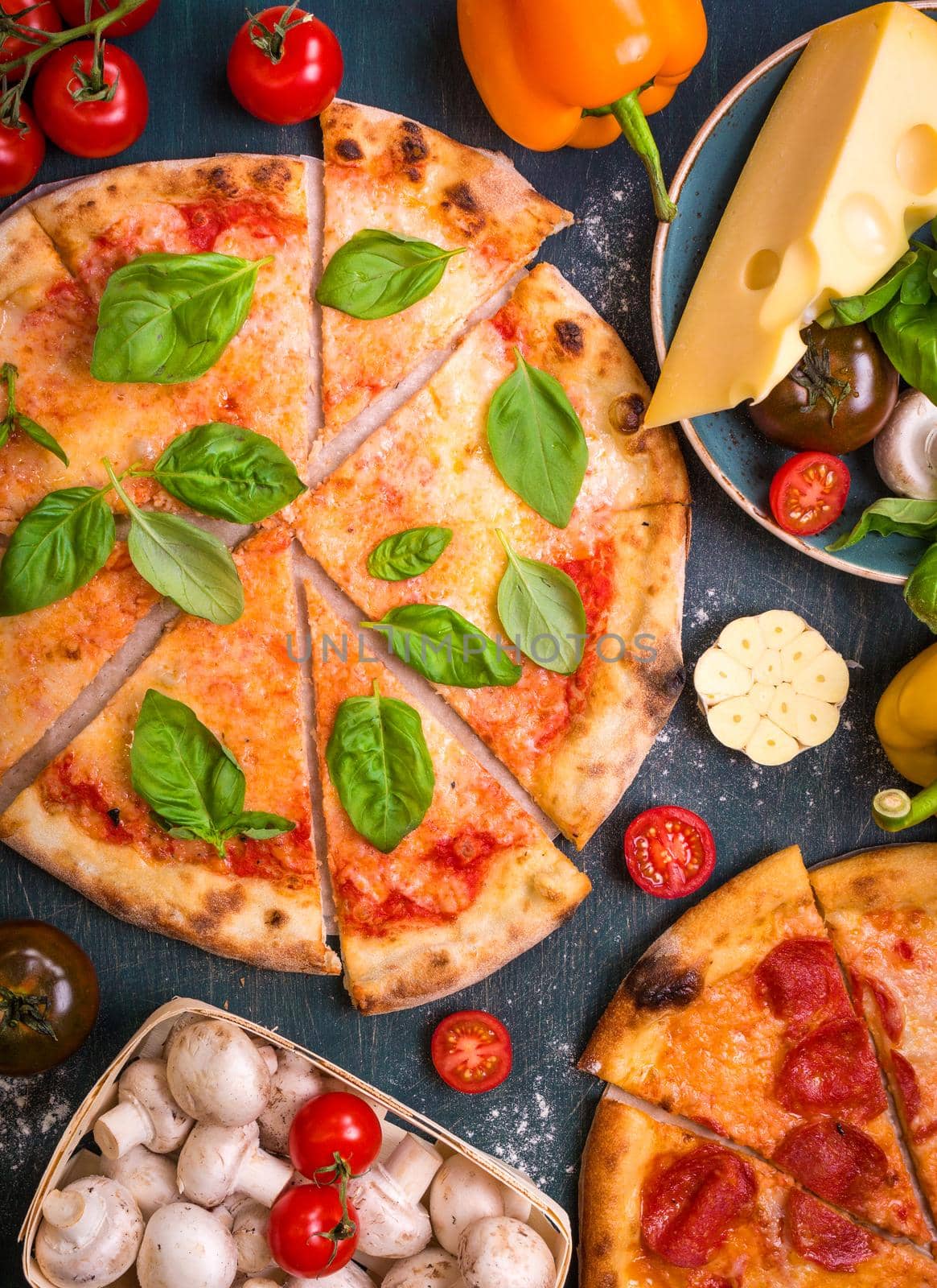 Delicious sliced pizza and ingredients for making pizza. Flour, cheese, tomatoes, basil, pepperoni, mushrooms and rolling pin over wooden background. Top view. Pizza ready to eat