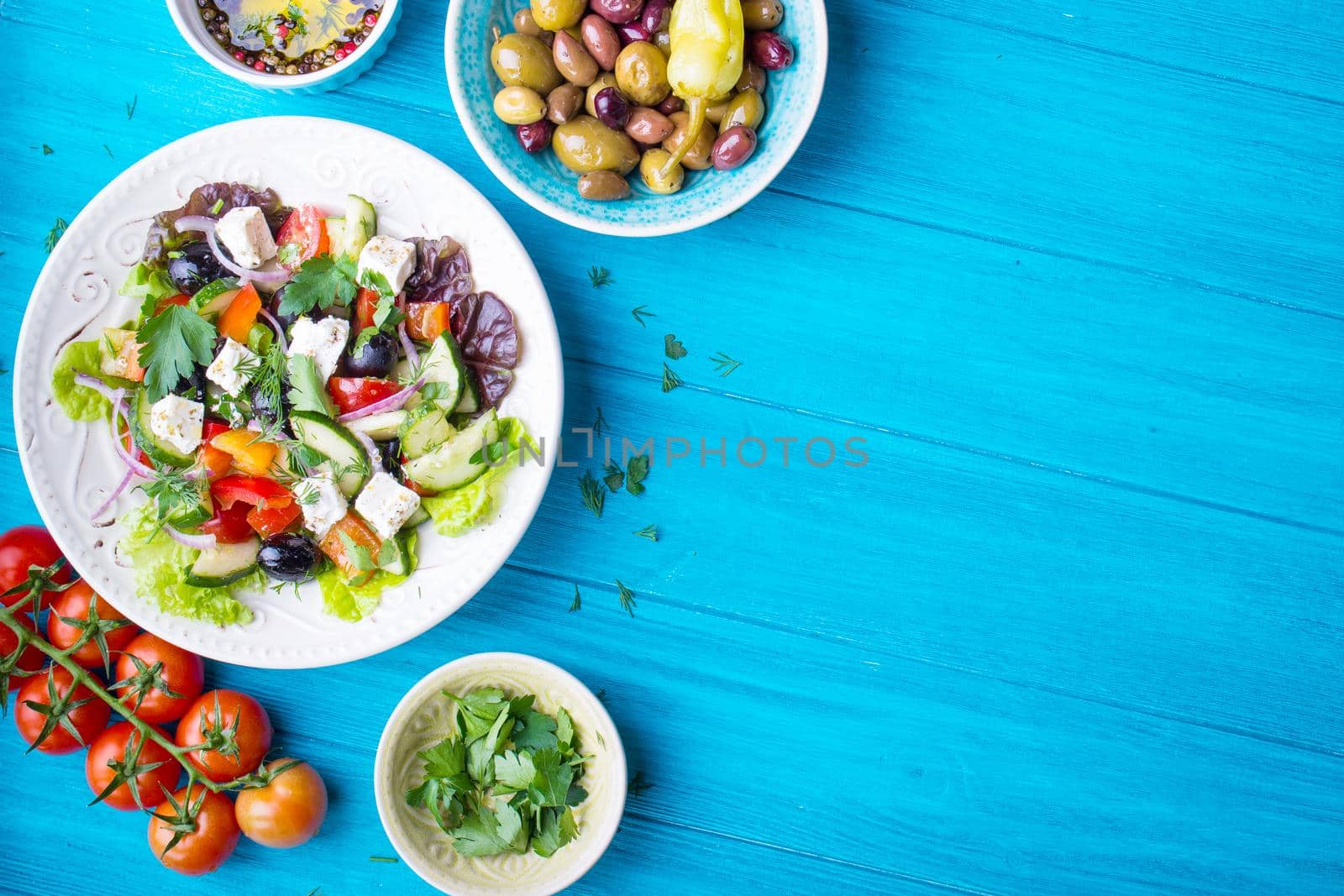 Greek salad background. Bowl with fresh greek salad, tomatoes, olives, olive oil on wooden table. Space for text. Top view. Traditional greek dish. Ingredients for making salad. Mediterranean diet