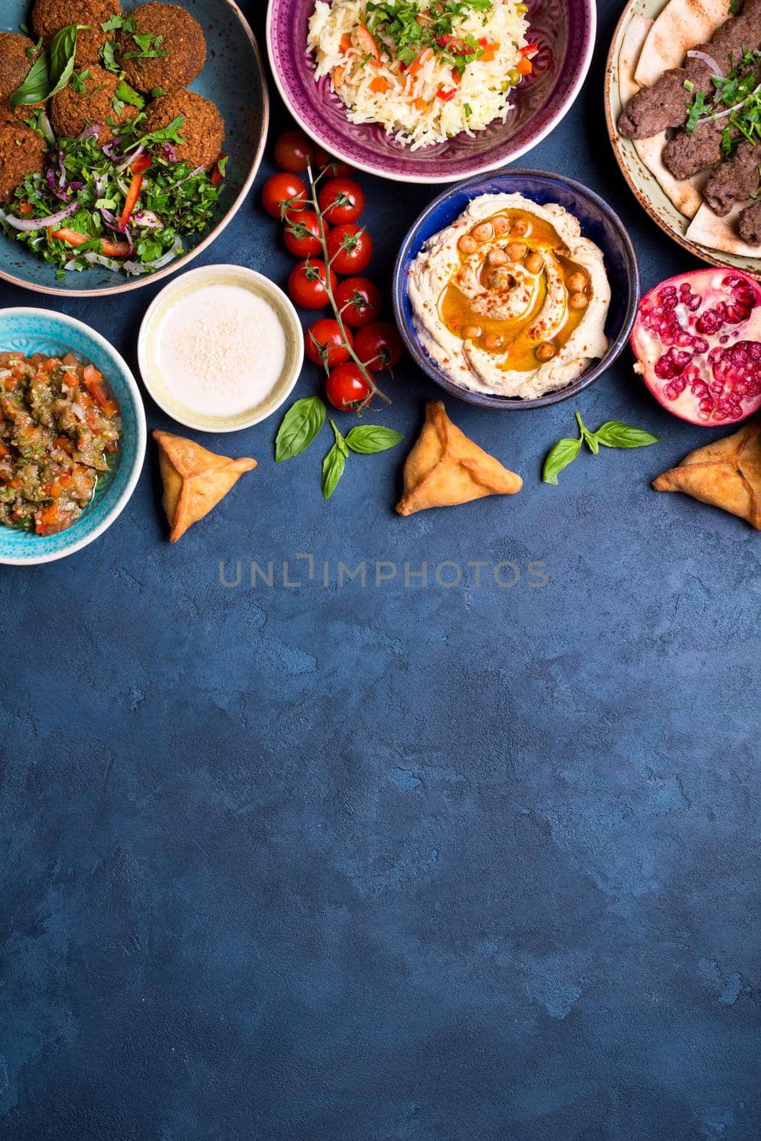 Middle eastern or arabic dishes and assorted meze on concrete rustic background. Meat kebab, falafel, baba ghanoush, hummus, sambusak, rice, tahini, kibbeh, pita. Halal food. Space for text. Top view