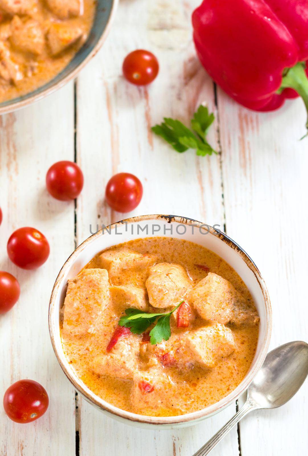 Delicious chicken stew with paprika in a bowl on a white wooden table. With fresh cherry tomatoes, red bell pepper and parsley. Traditional hungarian dish paprikash. Comfort food. Selective focus