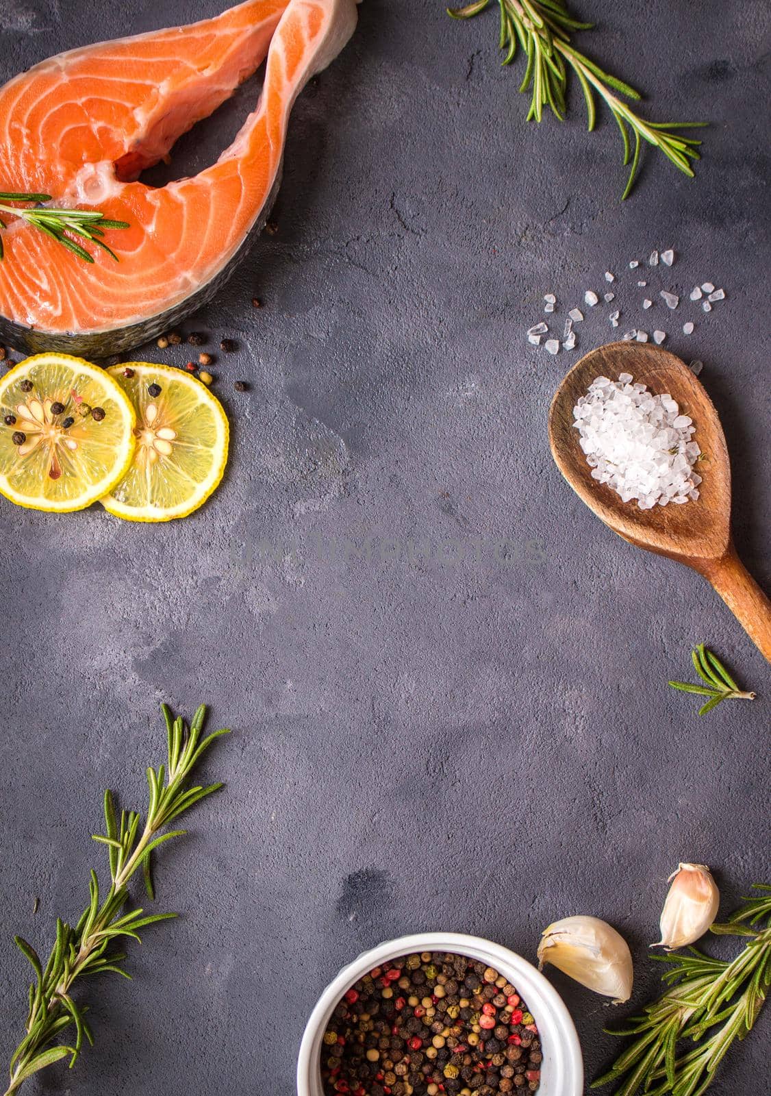 Fresh raw salmon steak, lemon, herbs, spices, wooden spoon on dark rustic concrete background. Food frame. Ingredients set for making healthy dinner. Healthy/diet concept. Space for text. Fresh fish