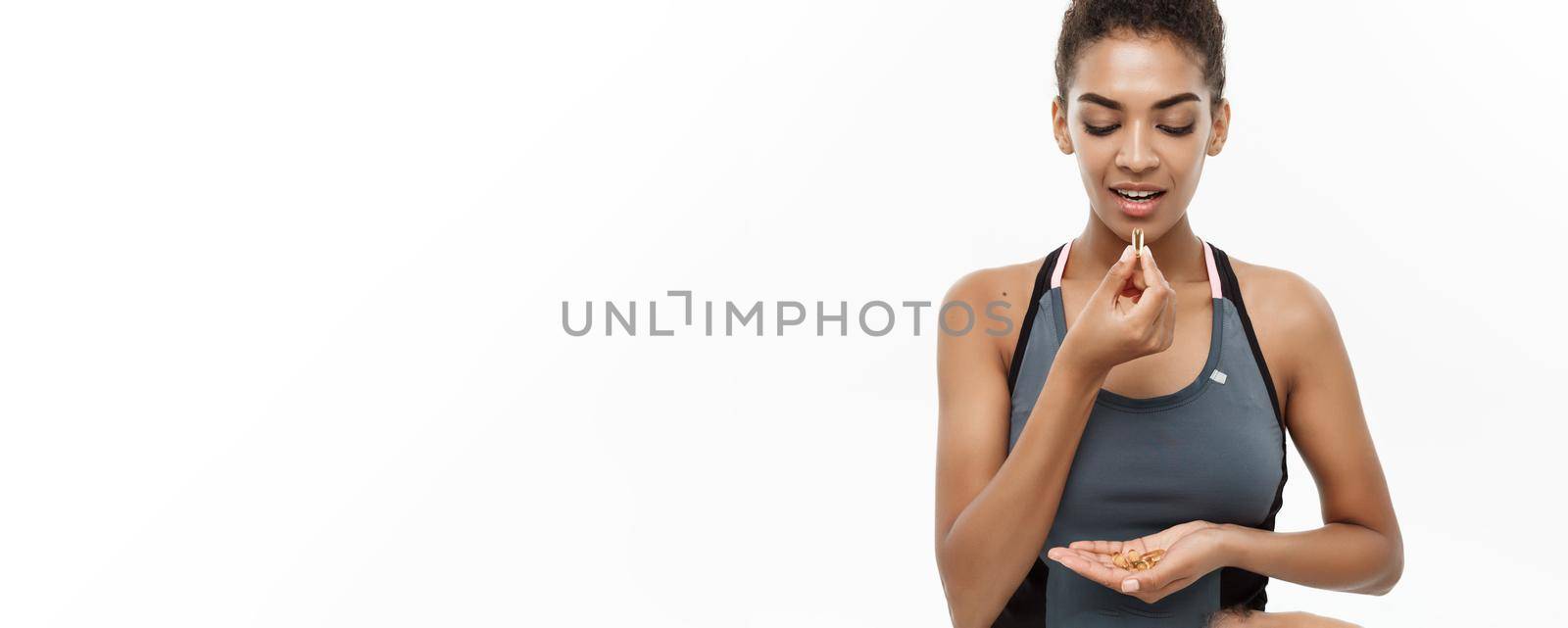 healthcare concept - Closeup portrait of beautiful African American taking a pill of Cod liver oil. Isolated on white studio background.