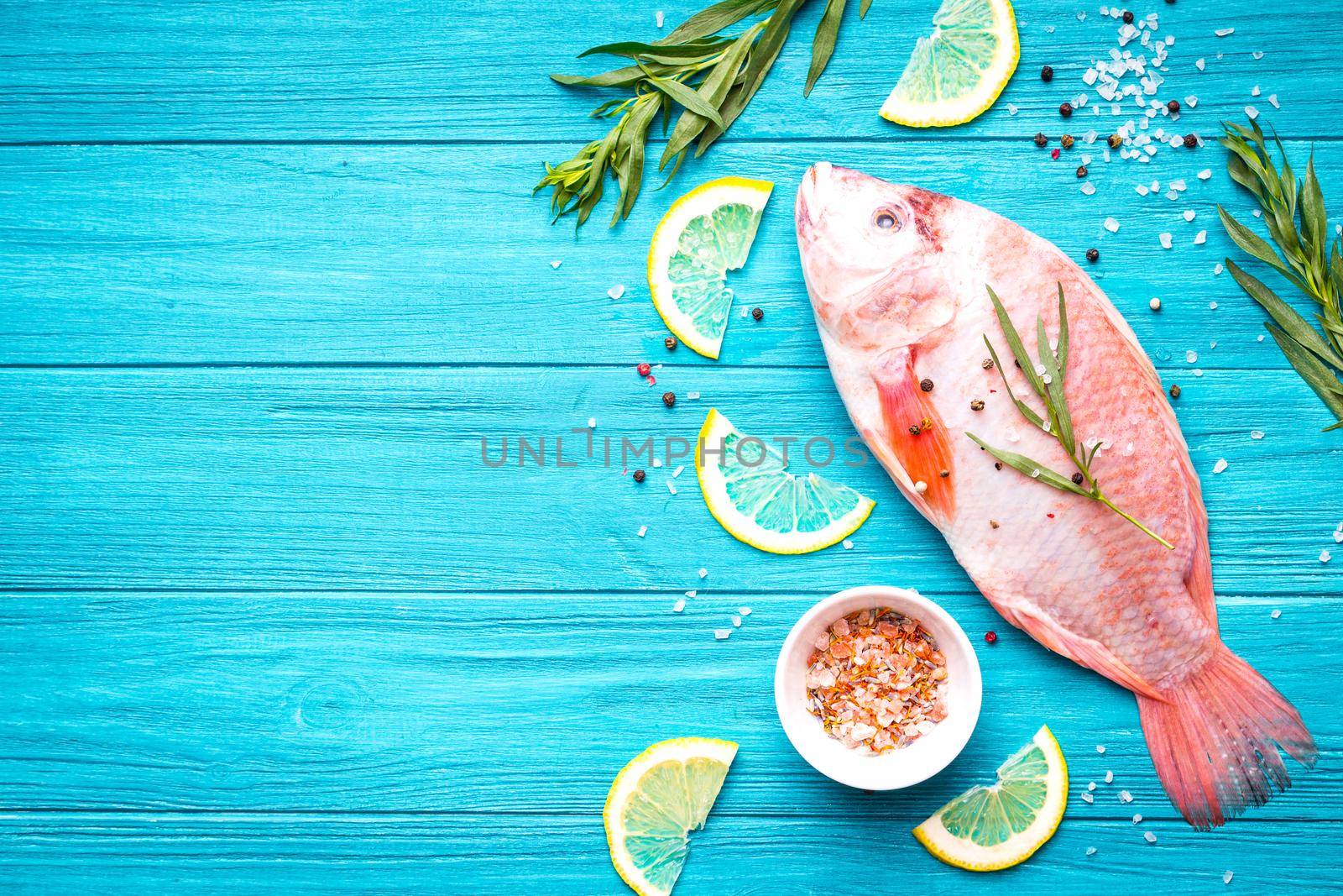 Fresh fish tilapia ready to cook. Raw fish with herbs, lemon, salt, pepper on wooden rustic background. Ingredients for cooking or making healthy dinner. Fish background. Space for text. Diet/healthy