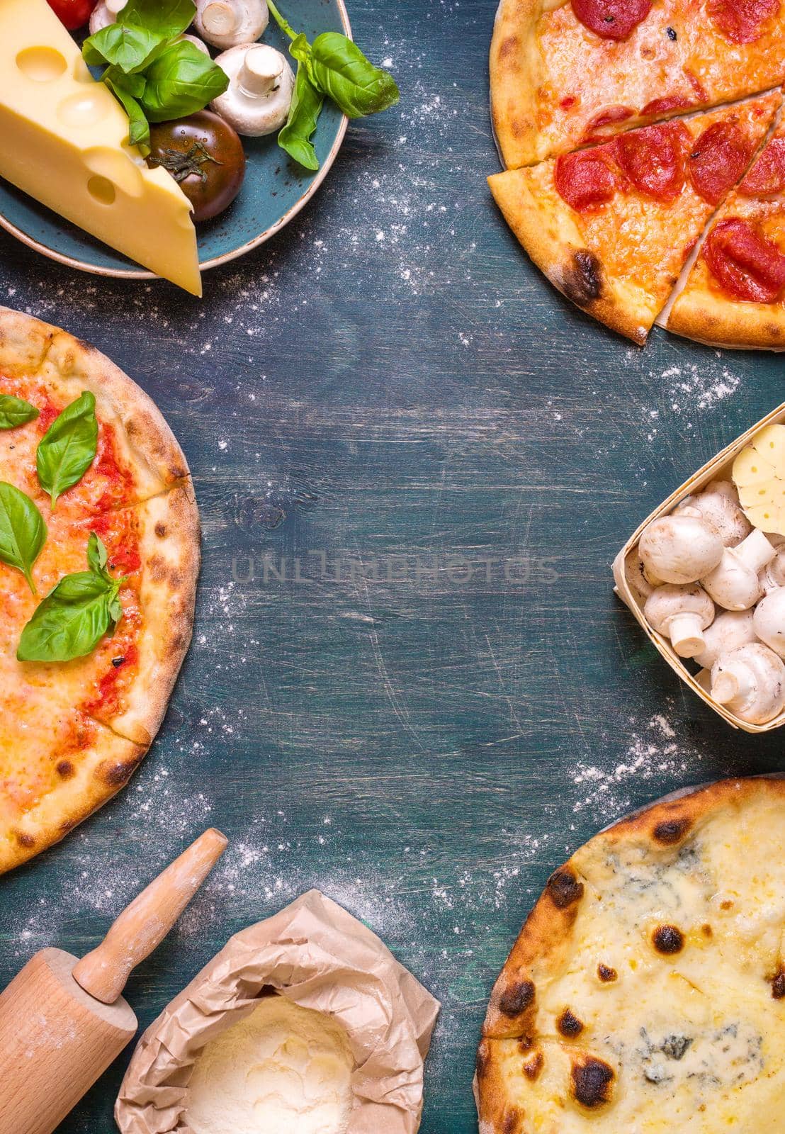 Pizza with assorted toppings and ingredients background. Space for text. Pizza, flour, cheese, tomatoes, basil, pepperoni, mushrooms and rolling pin over old wooden background. Top view. Food frame