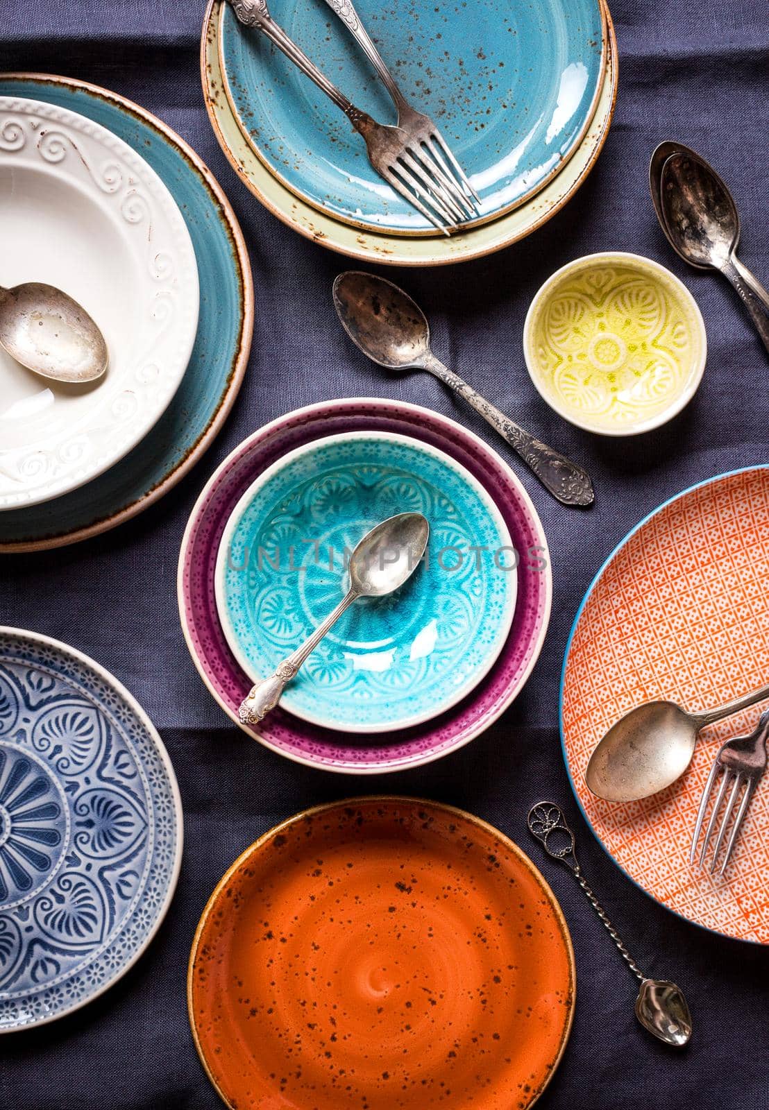 Vintage multicolored empty plates and bowls on a dark gray linen tablecloth. With antique spoons and forks. Table setting. Shabby chic/retro style. Top view. Rustic kitchen