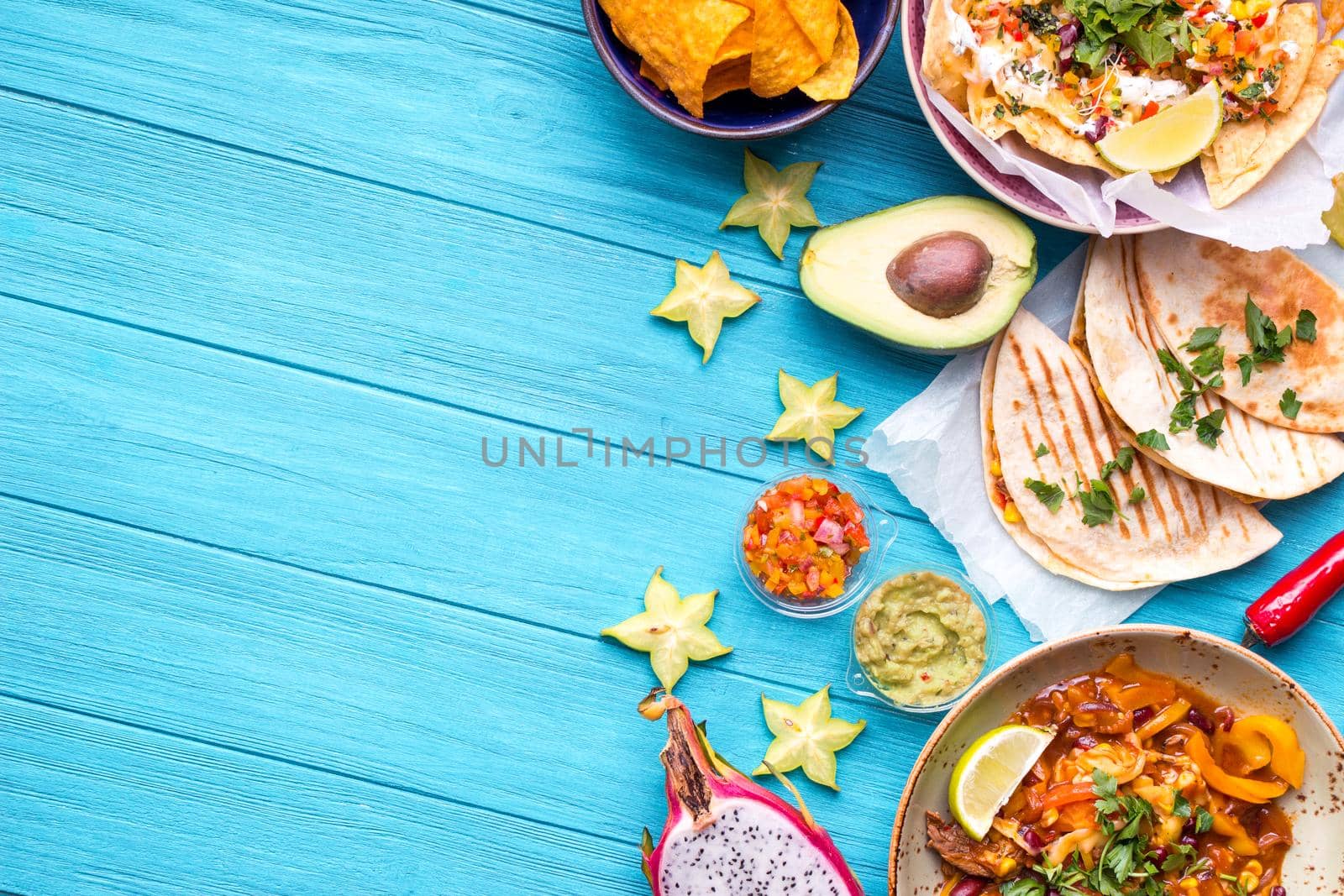 Traditional Mexican food background. Table with different Mexican dishes. Cheese nachos, tacos, guacamole, fajitas, tortilla chips, Mexican fruits. Tex-Mex cuisine. Space for text. Mexico/Texas style