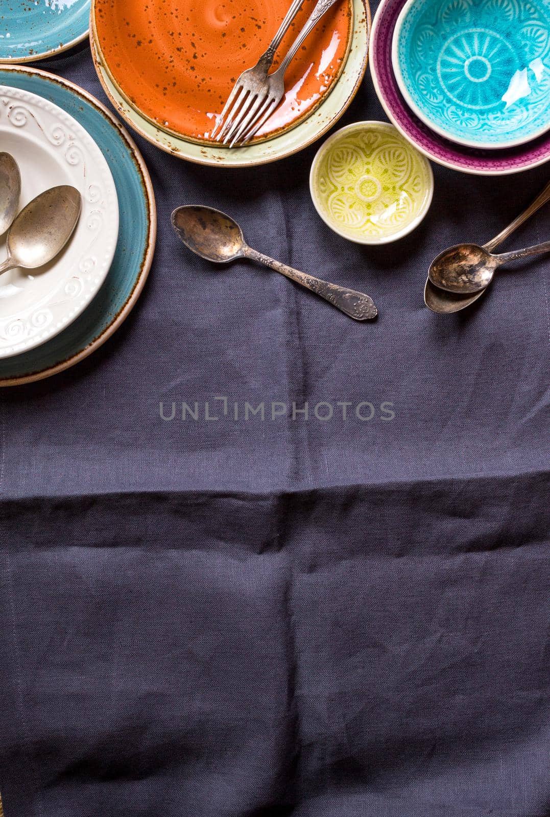 Vintage multicolored empty plates and bowls on a gray linen tablecloth. With antique spoons and forks. Space for text. Table setting. Shabby chic/retro style. Top view. Rustic kitchen. Copy space
