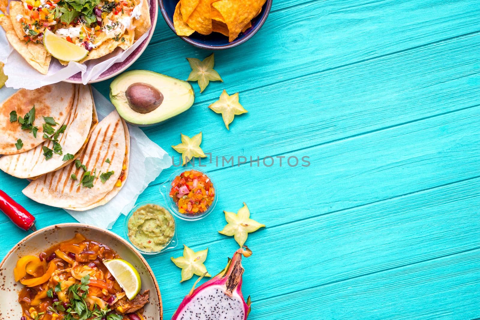 Traditional Mexican food background. Table with different Mexican dishes. Cheese nachos, tacos, guacamole, fajitas, tortilla chips, Mexican fruits. Tex-Mex cuisine. Space for text. Mexico/Texas style