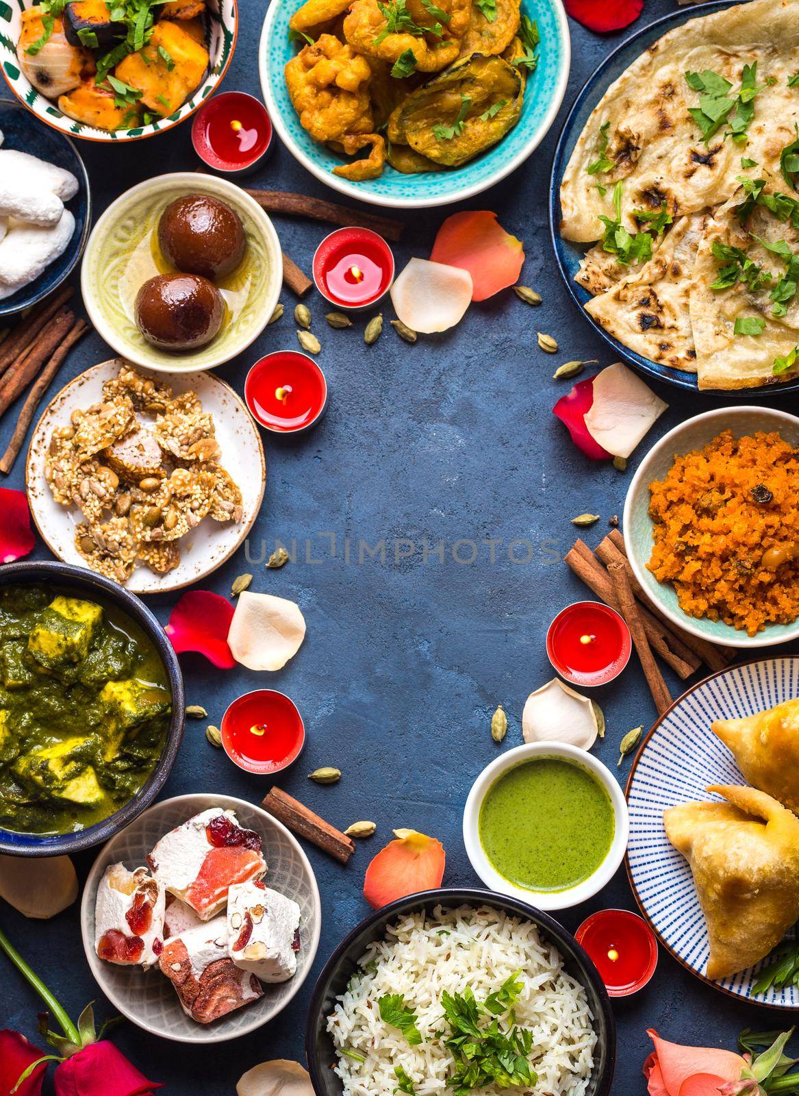 Festive food for Indian festival Diwali. Naan, samosa, rice, paneer, sweets. Background. Holiday Indian table with food, sweets, flowers, burning candles. Diwali celebratory dinner. Space for text.