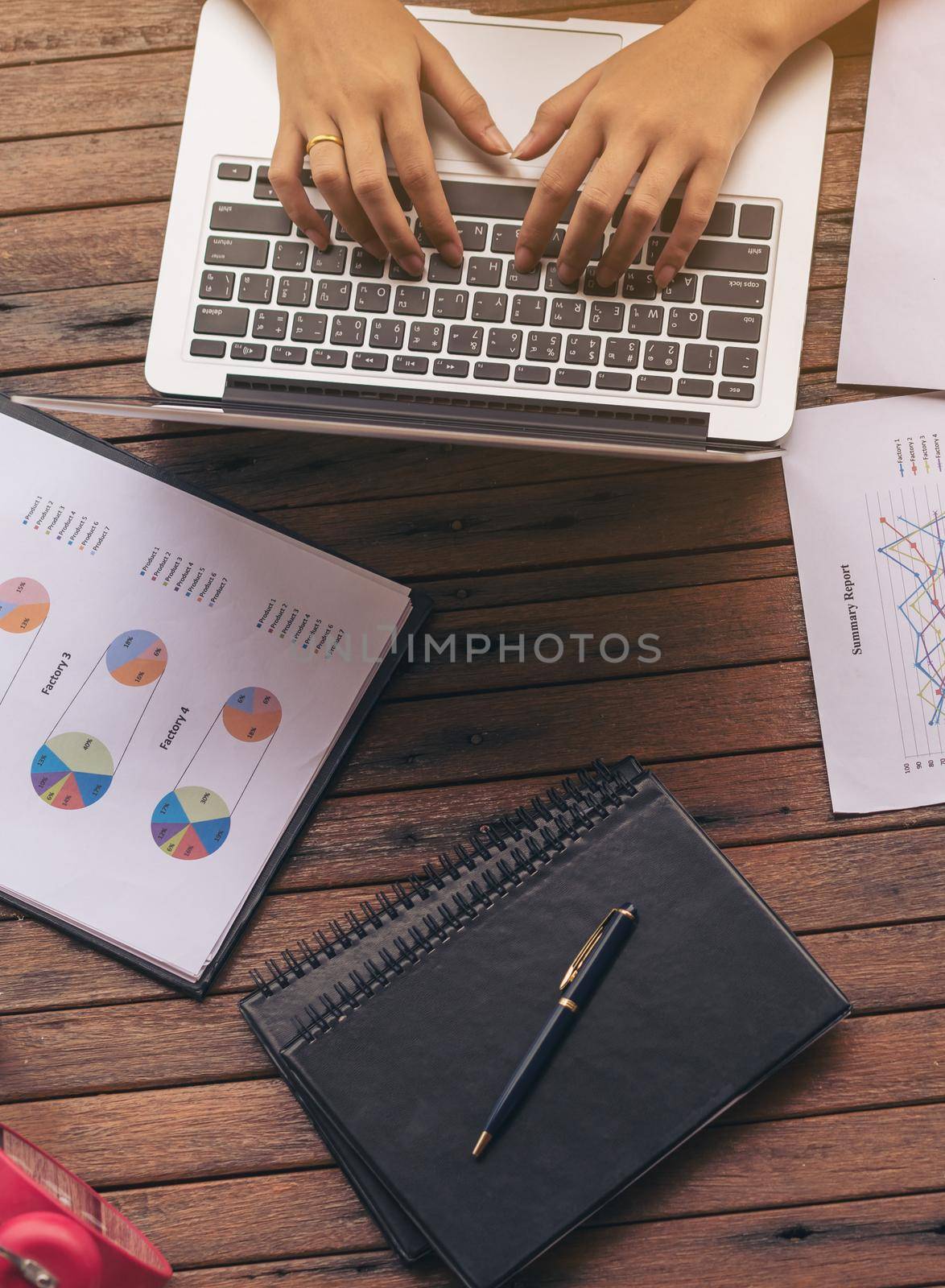 Woman's hand typing on laptop computer. Business report, mobile phone and business summary laid on desk. Online and internet for business connectivity. Business work at home office. Business concept.