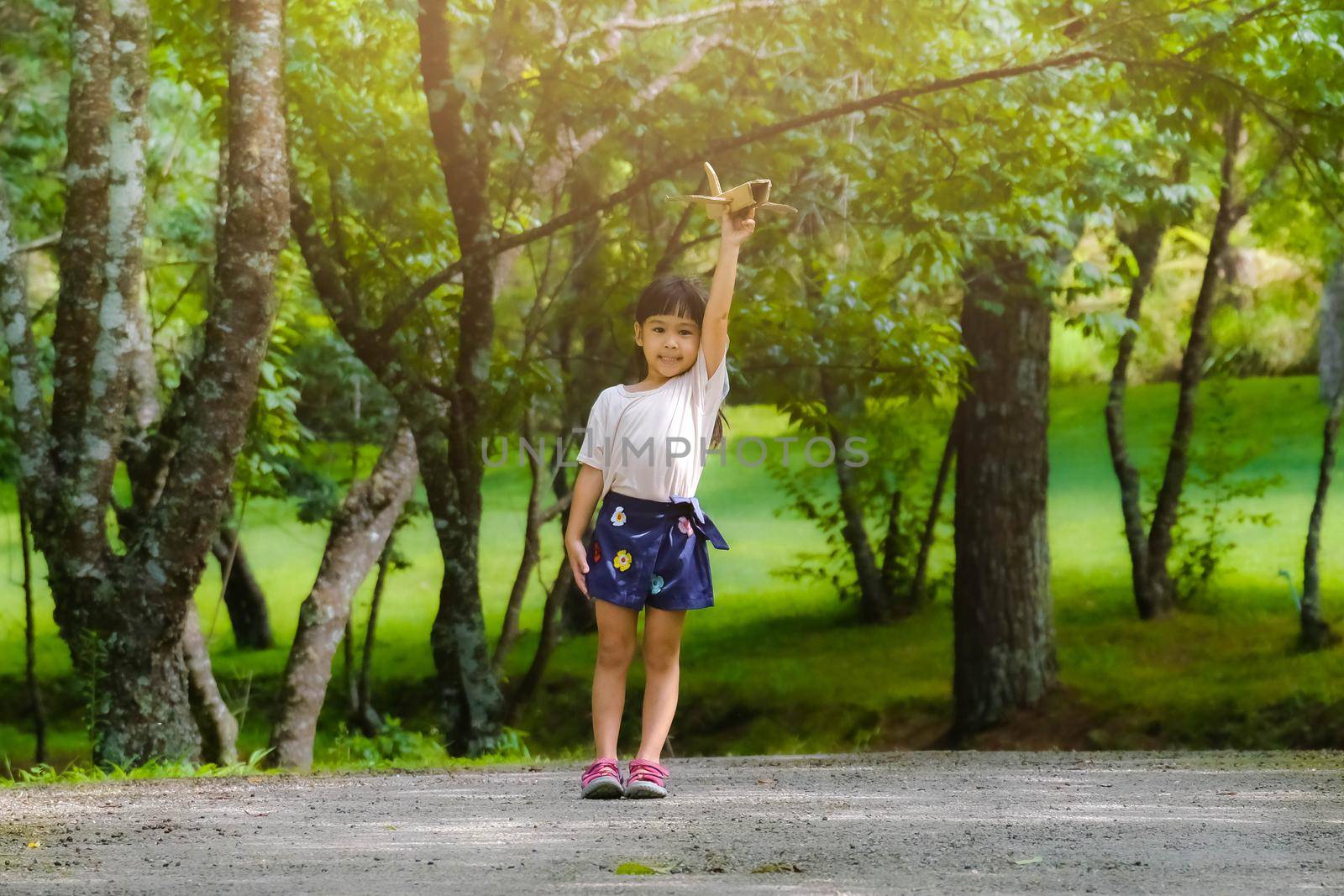 Happy little girl playing with airplanes made of cardboard in summer park. Cute girl with a toy airplane running on the road in the park. Happy childhood concept.