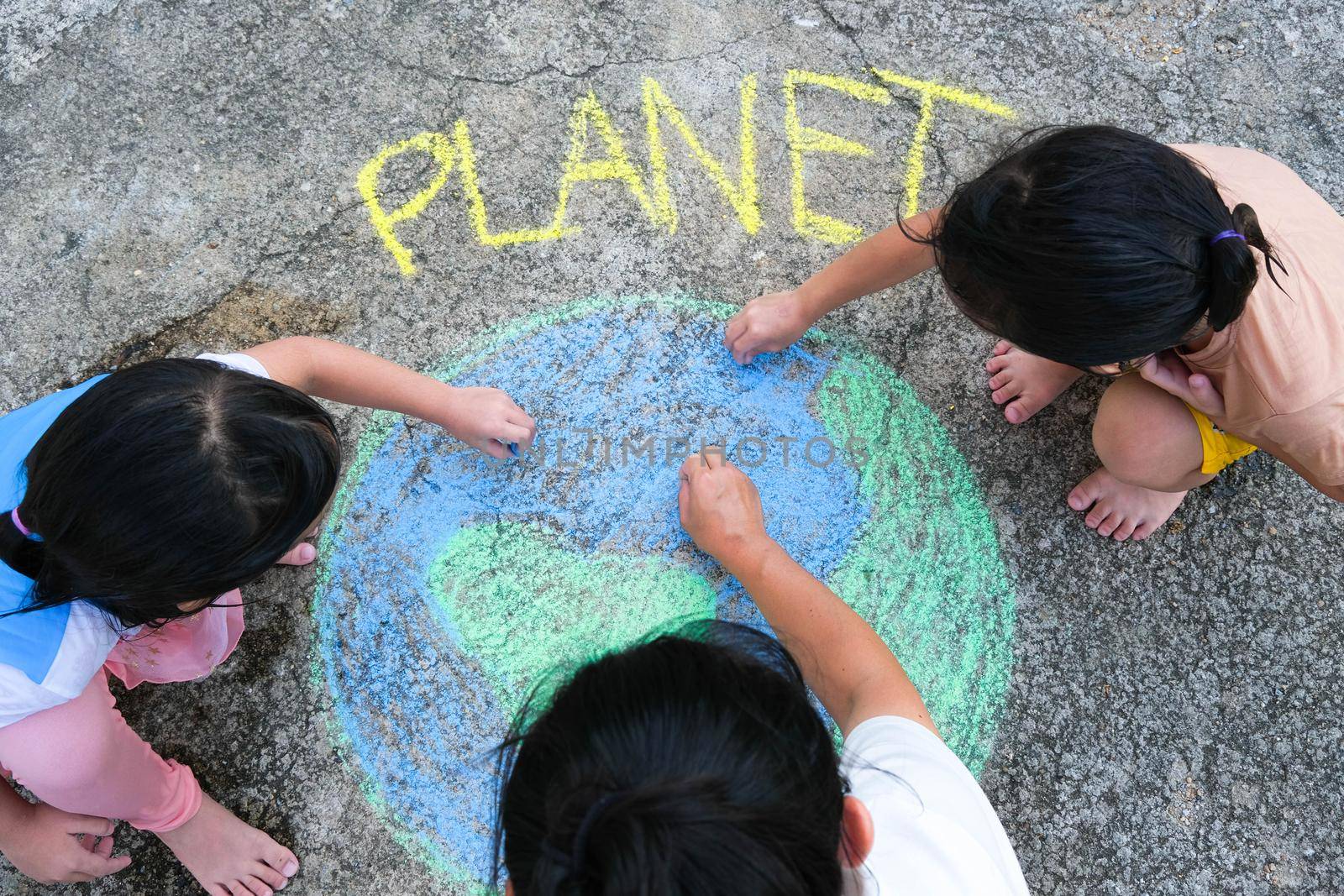 Volunteer family paints a beautiful world with the message Planet on asphalt. Little children and young woman drawing with colorful chalk on courtyard. Concept of world environment day. by TEERASAK