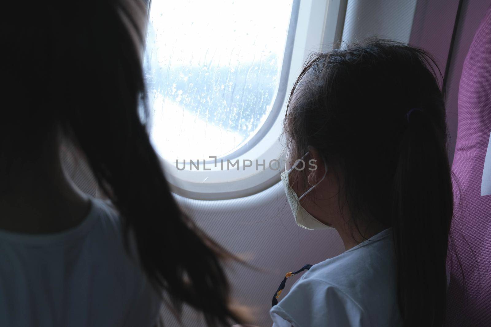 Child in airplane window seat. Two cute little sisters are watching the sky and clouds outside the plane window as they sit on the plane seat. Travel and family vacation. by TEERASAK
