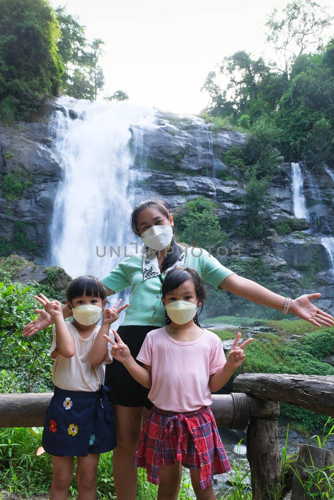 Family of Asian tourists standing near Wachirathan Waterfall looking at camera and smiling in Inthanon National Park, Chiang Mai, Thailand. by TEERASAK
