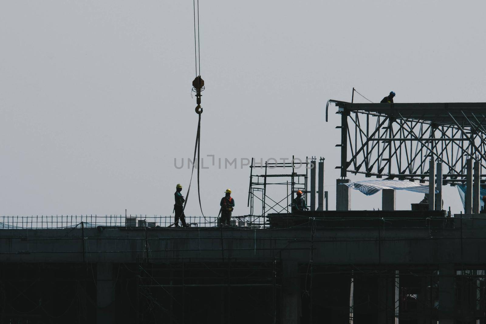 A large construction site with busy cranes. Tower cranes working on a construction site lifts a load at high-rise building in evening.