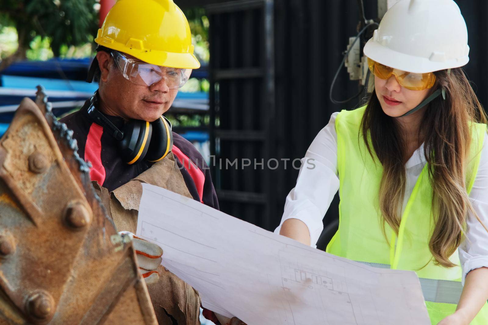 Asian engineering manager and mechanic worker working in a helmet while discussing and inspecting the manufacturing process in the factory. by TEERASAK
