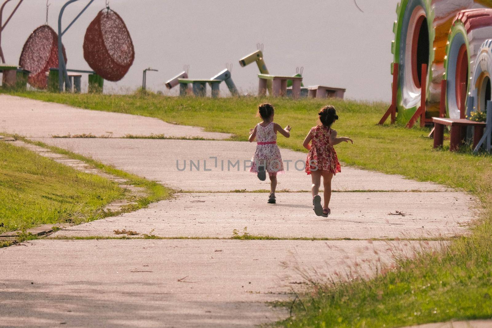 Rear view of children running on the road in the park. Two cute sisters are playing in the summer garden. Happy childhood concept.