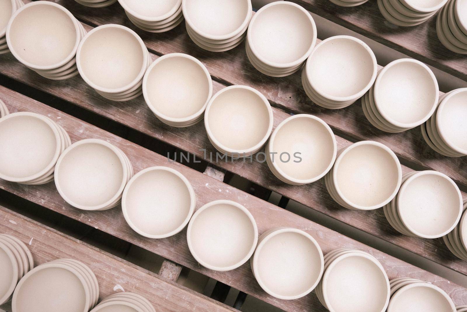 Many small round plates made of ceramic clay. Ceramic cup in rack prepare for painting design on surface in pottery workshop. handicraft and small business concept. by TEERASAK