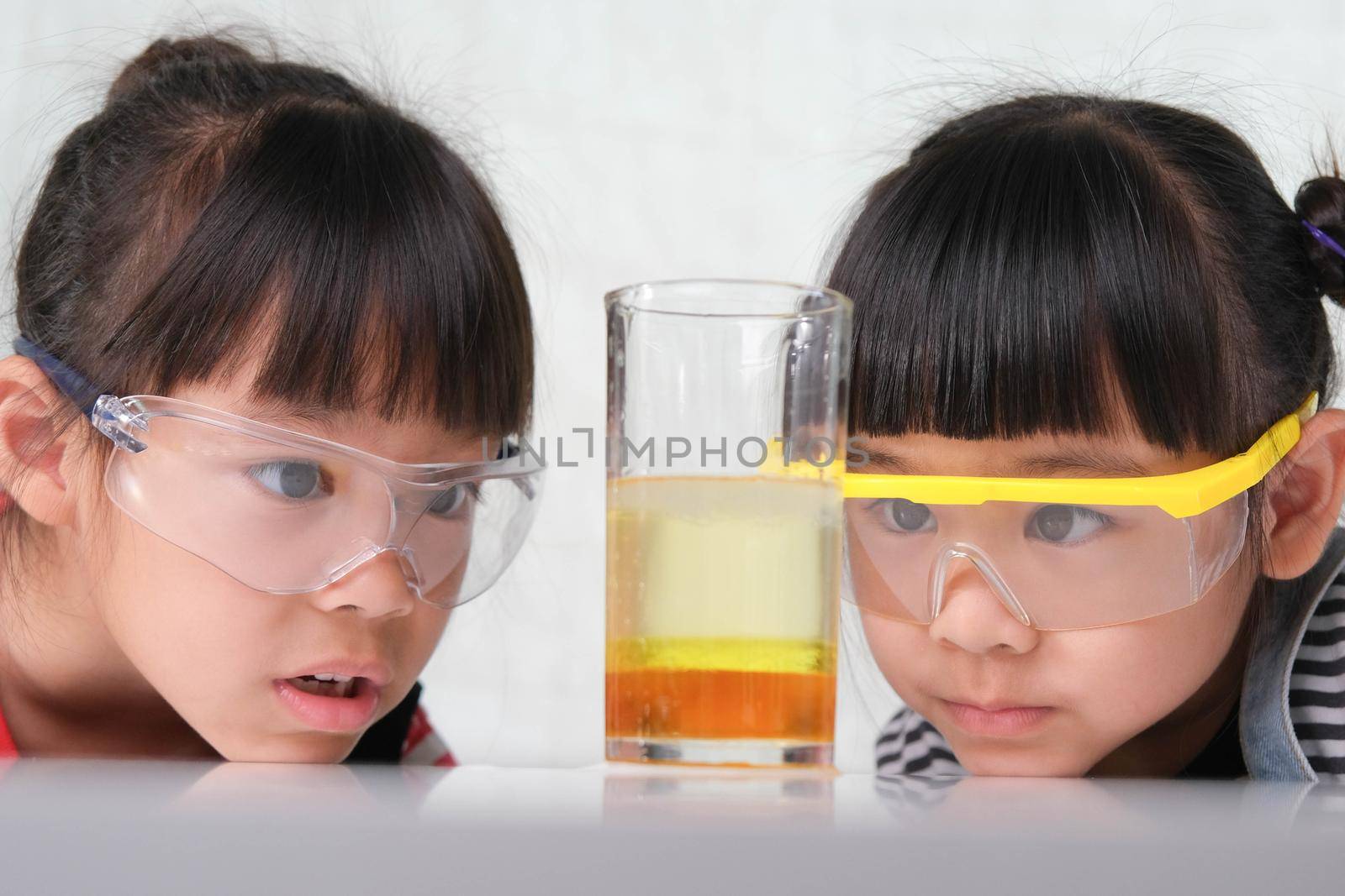 Children are learning and doing science experiments in the classroom. Two little sisters playing science experiment for home schooling. Easy and fun science experiments for kids at home. by TEERASAK