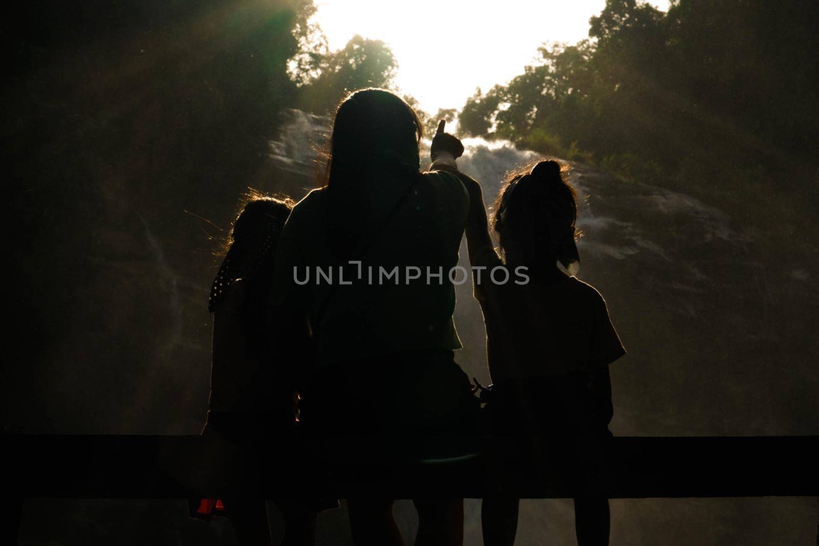 Family of Asian tourists standing near Wachirathan Waterfall looking at camera and smiling in Inthanon National Park, Chiang Mai, Thailand.