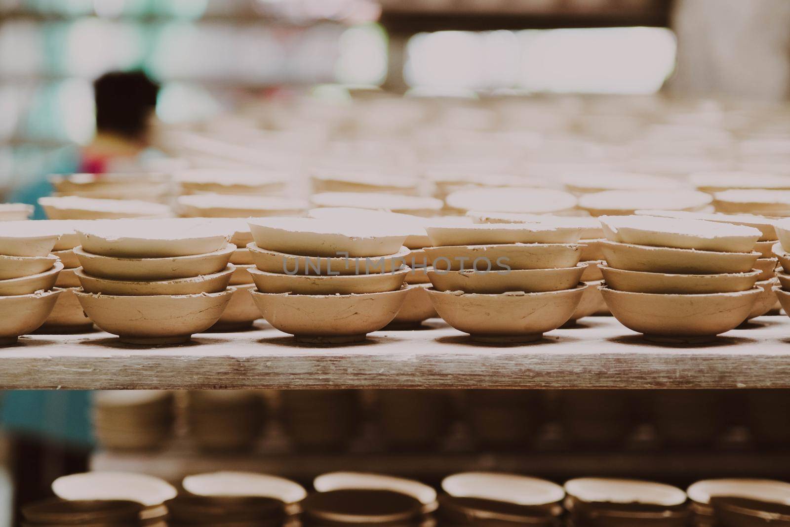 Many small round plates made of ceramic clay. Ceramic cup in rack prepare for cleans with sandpaper before applying the pattern on the clay product. handicraft and small business concept. by TEERASAK