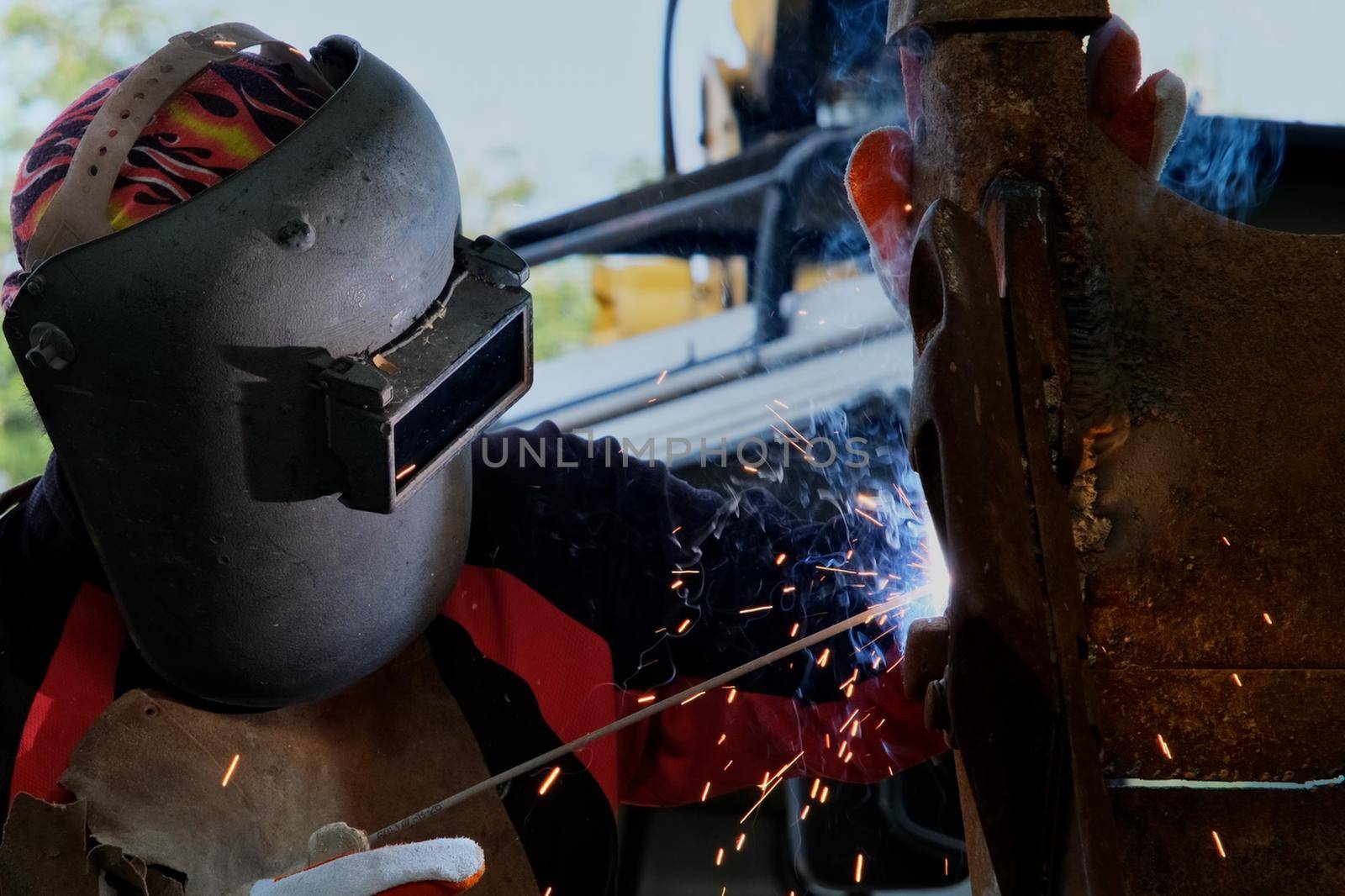 Skilled metalworkers wearing welding masks and gloves work in the home workshop with an arc welding machine. Worker welding metal with sparks, close-up by TEERASAK