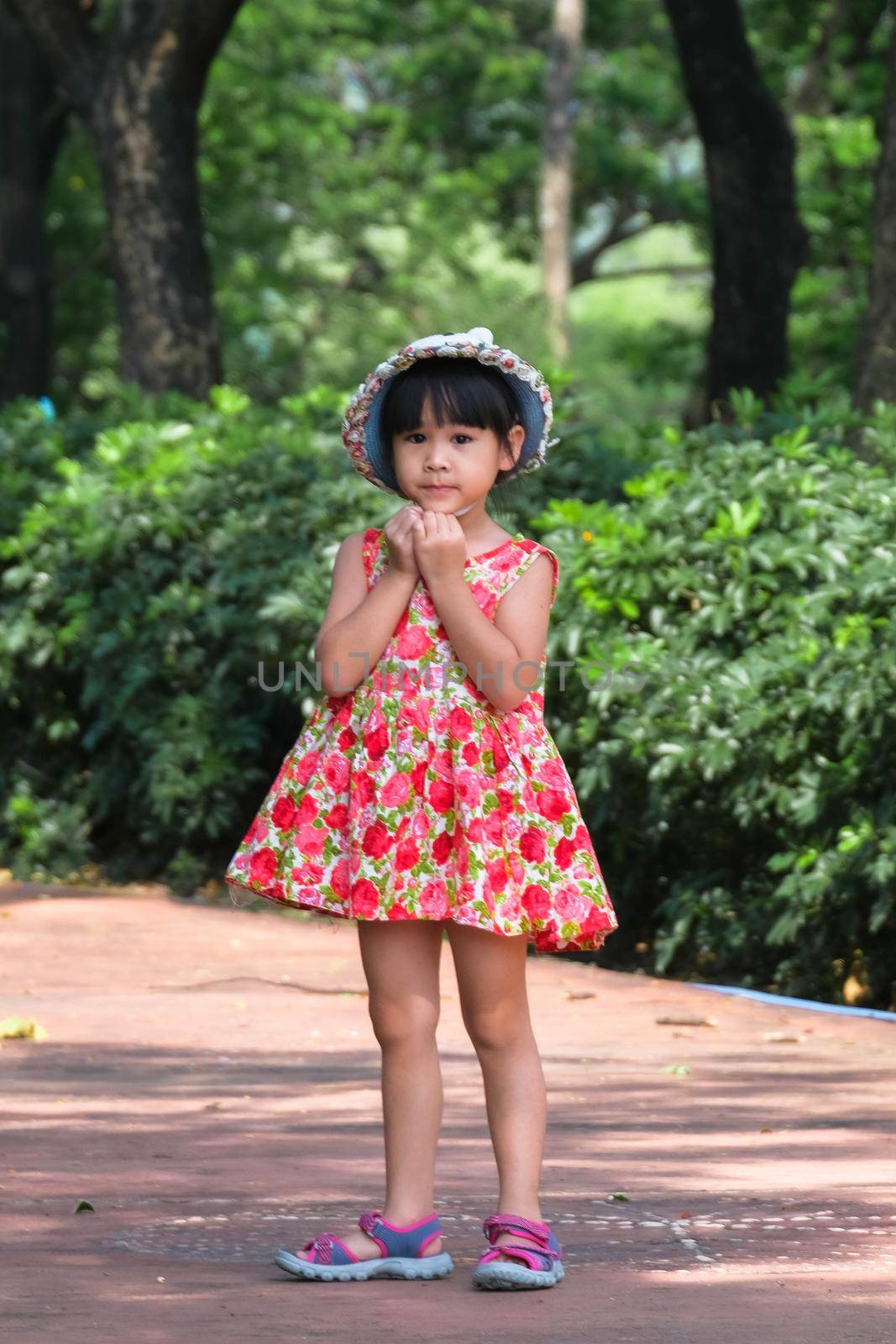 A cute smiling little girl in a red floral dress is walking and having fun on the green grass in the park. childhood concept by TEERASAK