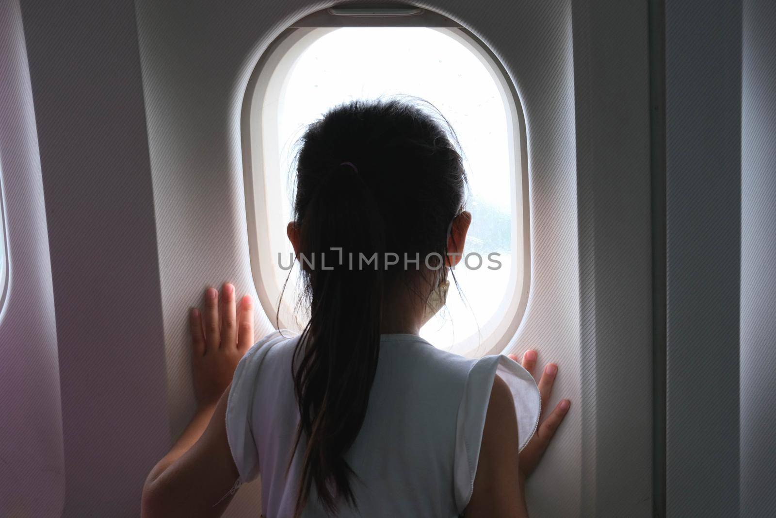 Cute little girl traveling by an airplane. Child girl looking aerial view of sky and cloud outside airplane window while sitting on airplane seat. travel concept