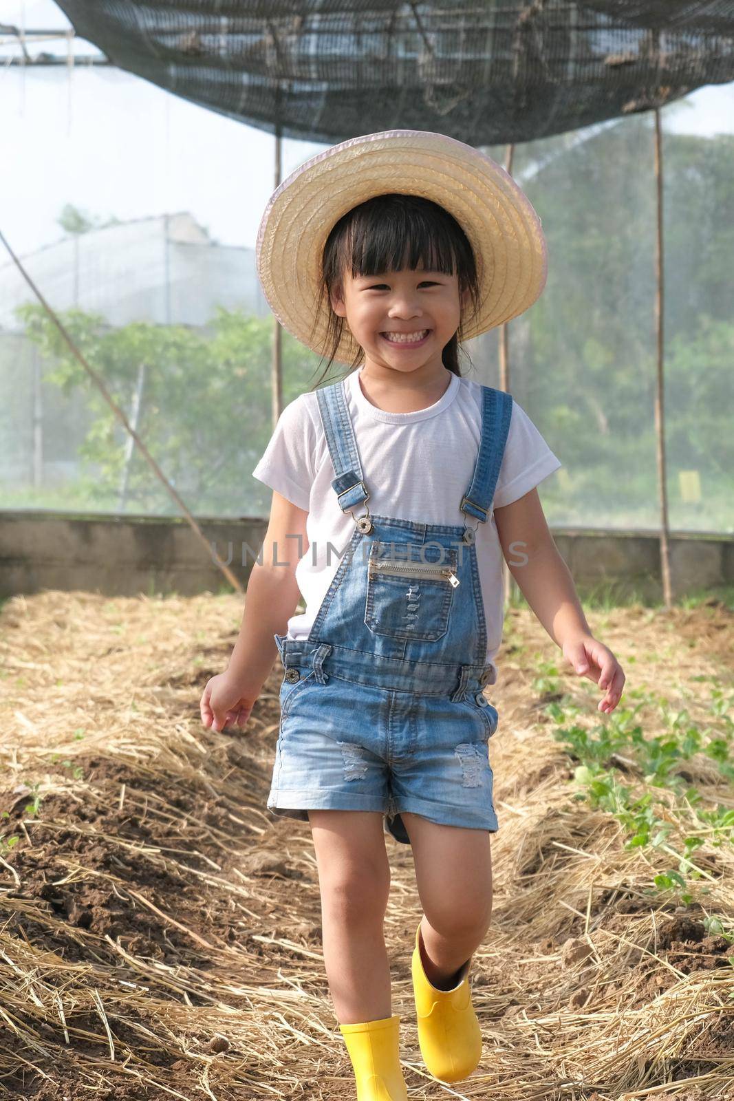 Little girl wearing a hat helps her mother in the garden, a little gardener. Cute girl playing in the vegetable garden.