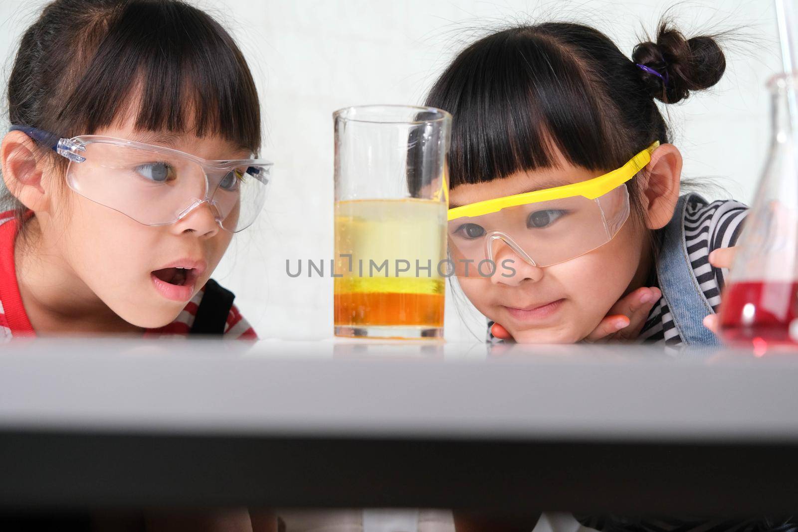 Children are learning and doing science experiments in the classroom. Two little sisters playing science experiment for home schooling. Easy and fun science experiments for kids at home. by TEERASAK
